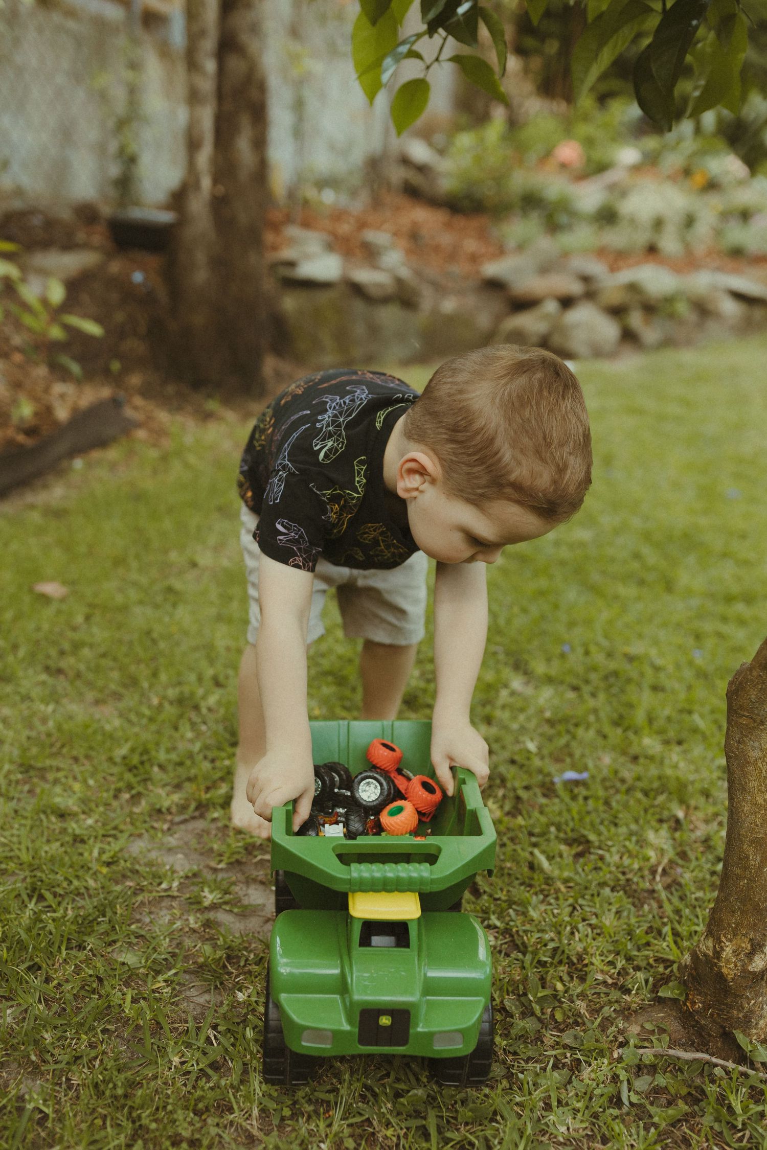 A child playing with a green toy tractor on grass.
