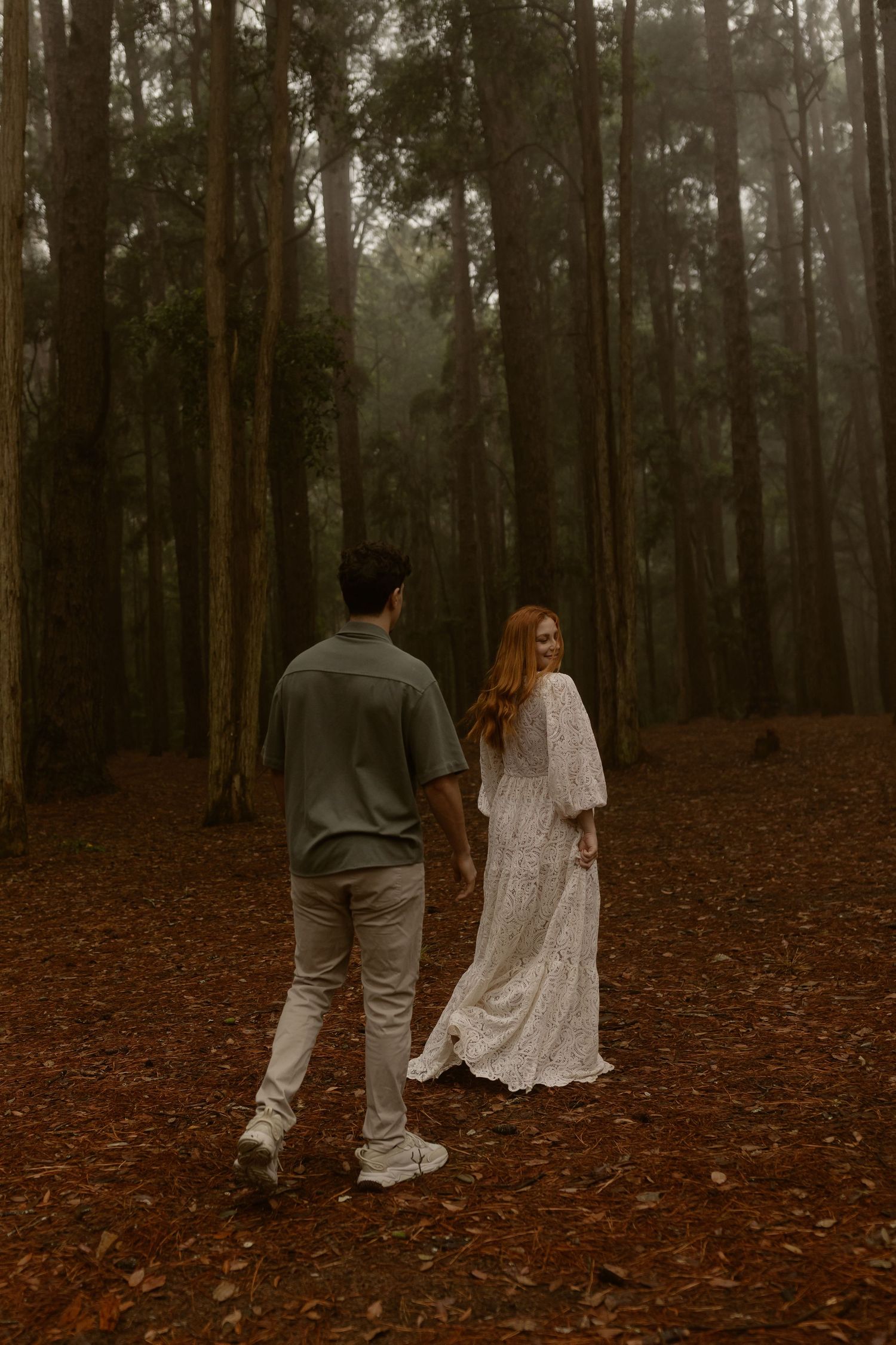 Two people walk through misty forest wearing contrasting white and gray outfits.
