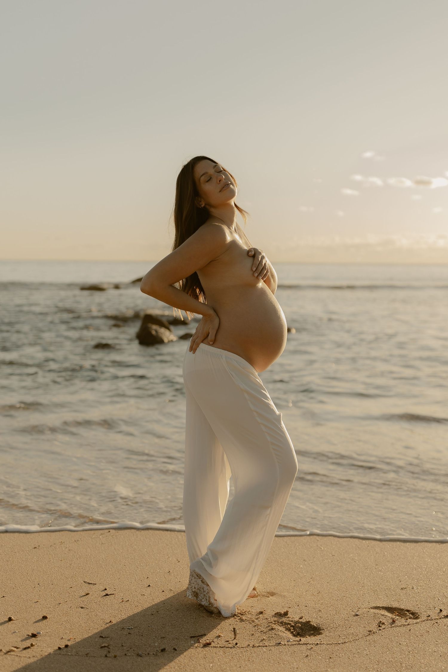 A person in white clothing strikes graceful poses on a beach at sunset.