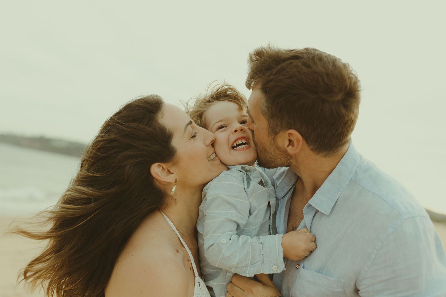 A family shares tender kisses and embraces on a sunny beach.