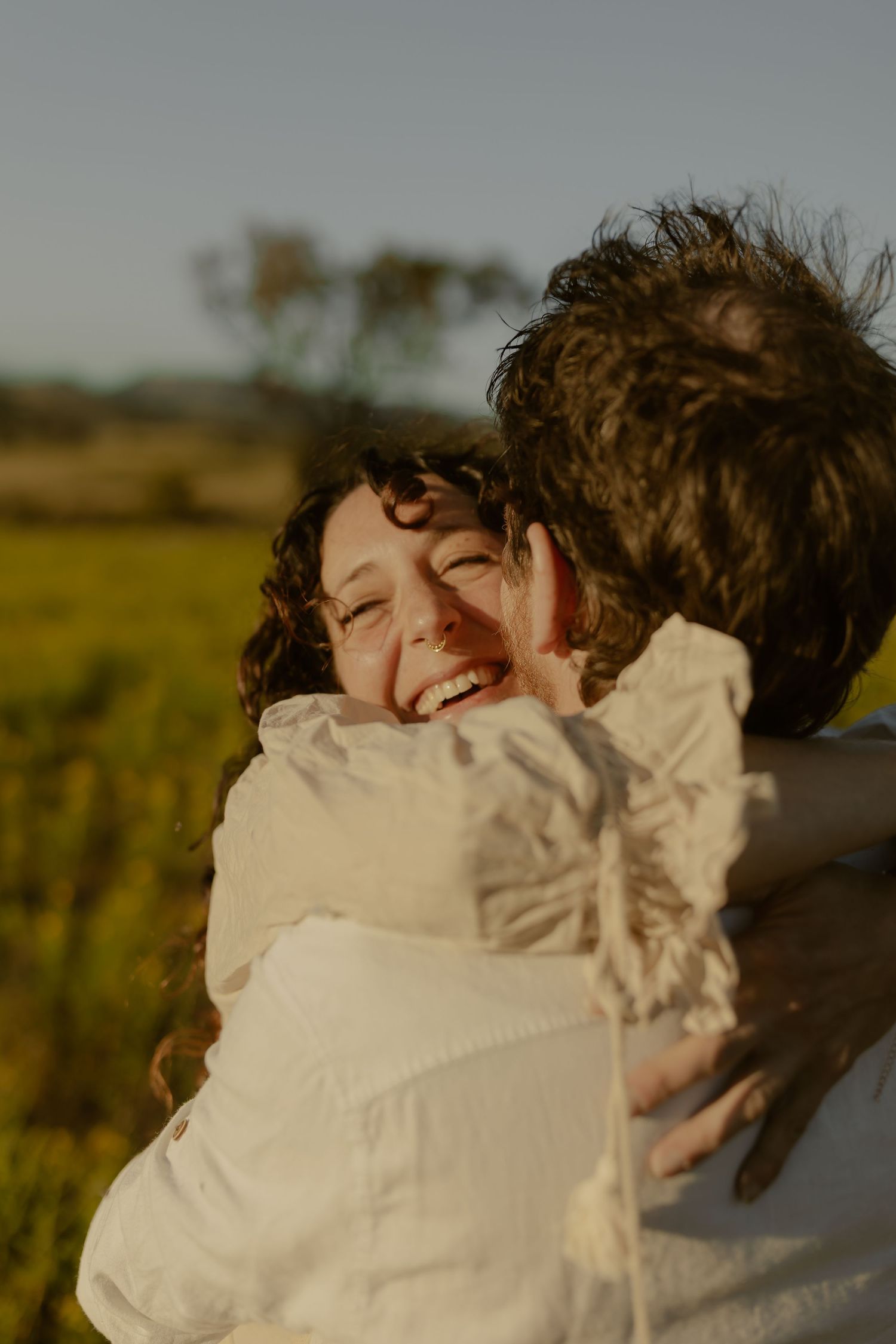 A joyful embrace captured in warm sunset light amidst a rural field setting.