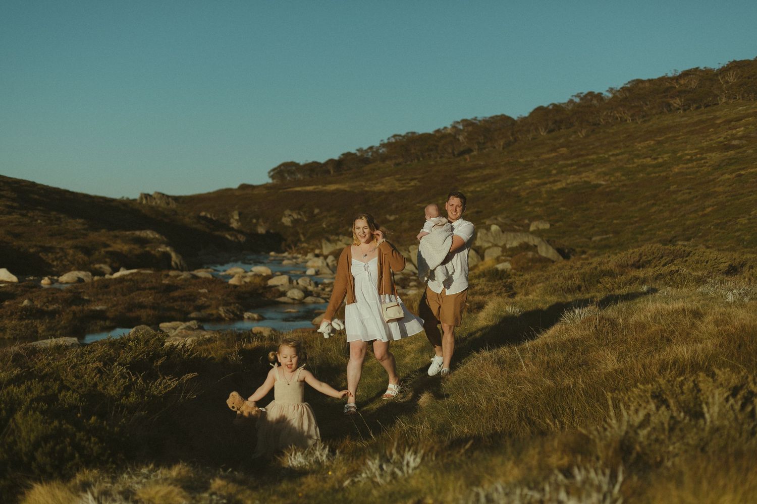 People enjoying a nature walk together along a scenic hillside trail with a stream and golden evening light.
