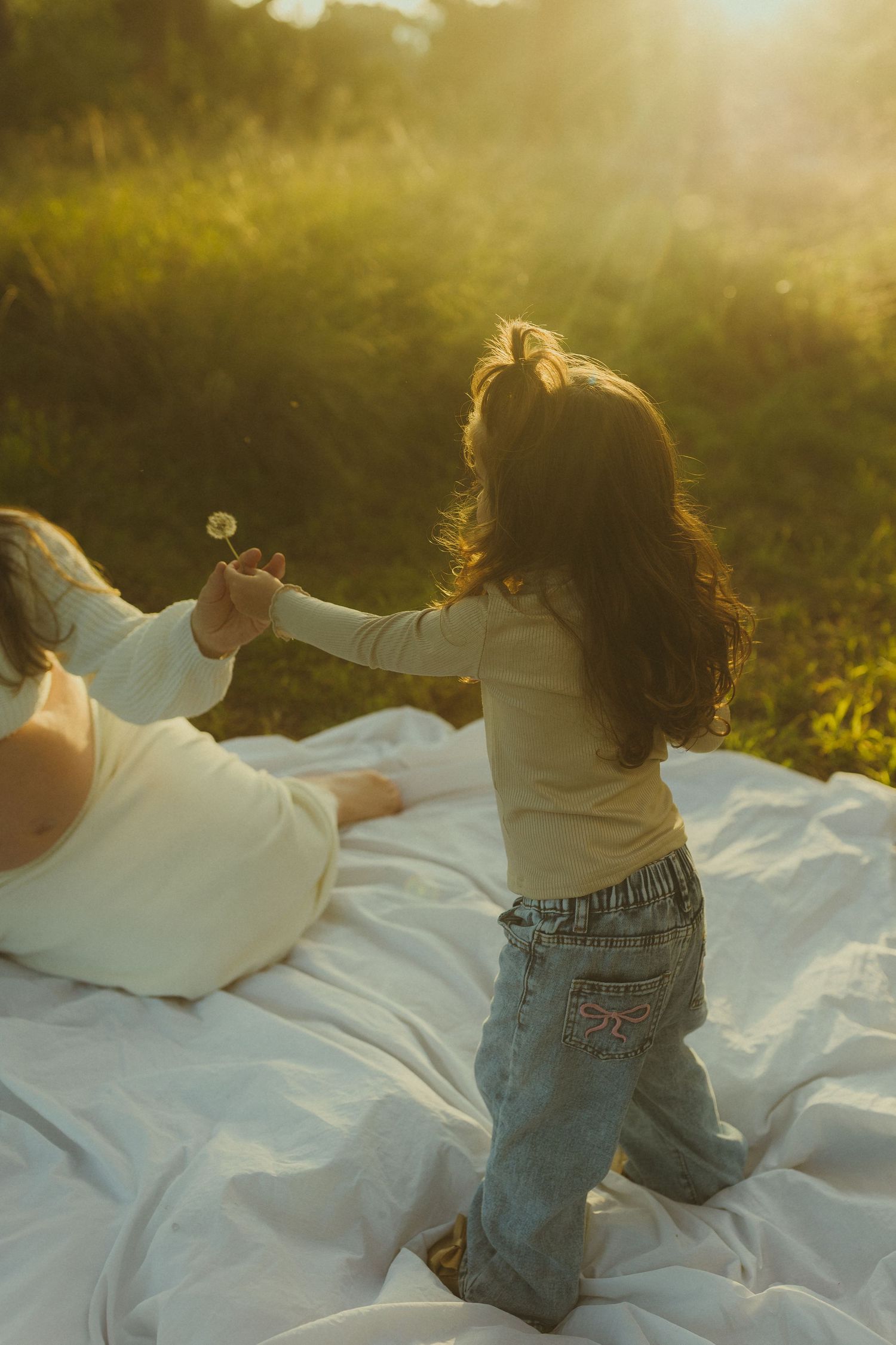 Child playing on a white blanket in a sunny meadow during sunset.