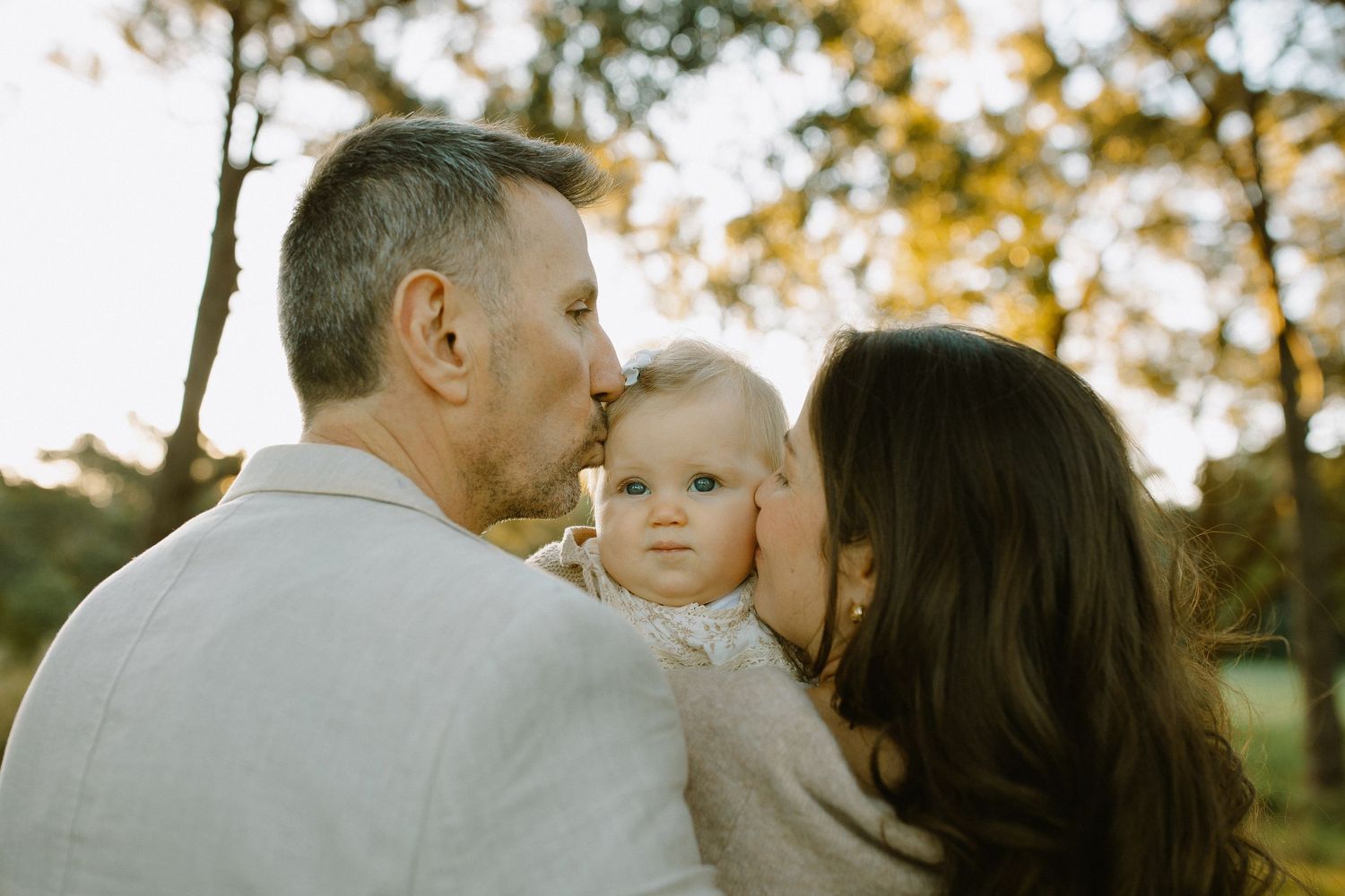 Intimate family moment outdoors with warm sunset lighting through trees.