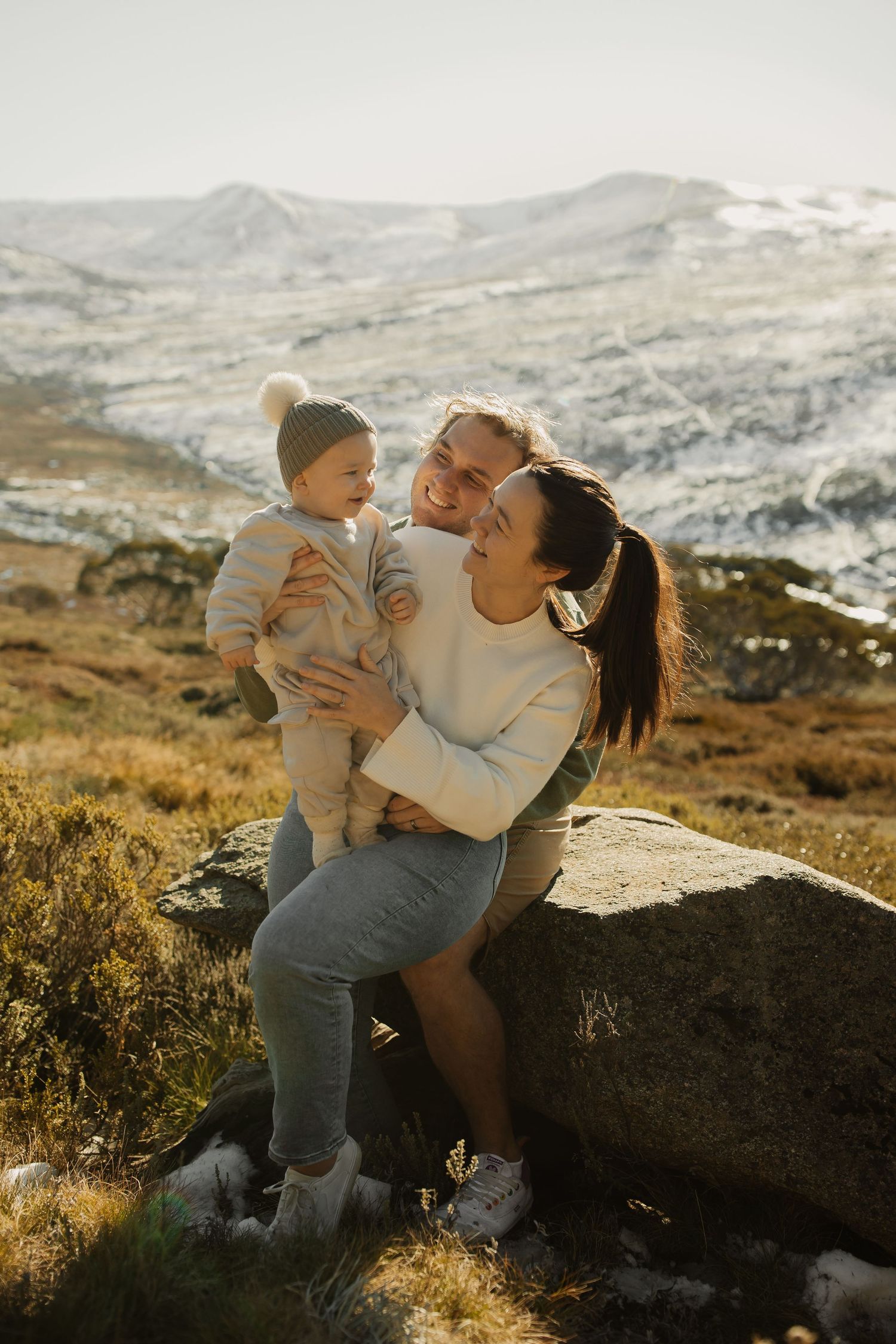 Family shares joyful moment together while sitting on rock in snowy mountain landscape at golden hour.