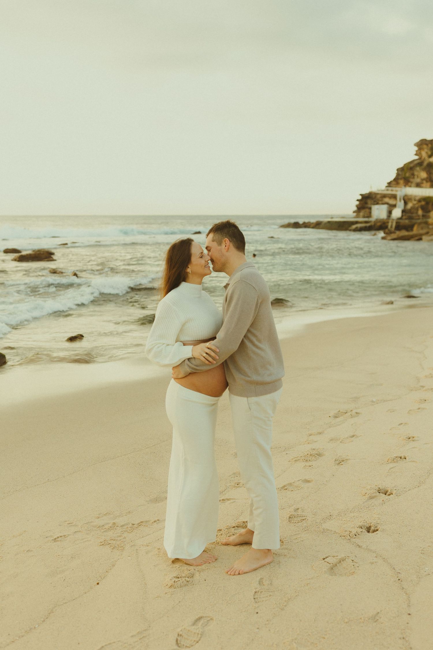 A romantic couple shares an intimate moment during their beachside maternity photo session at sunset.