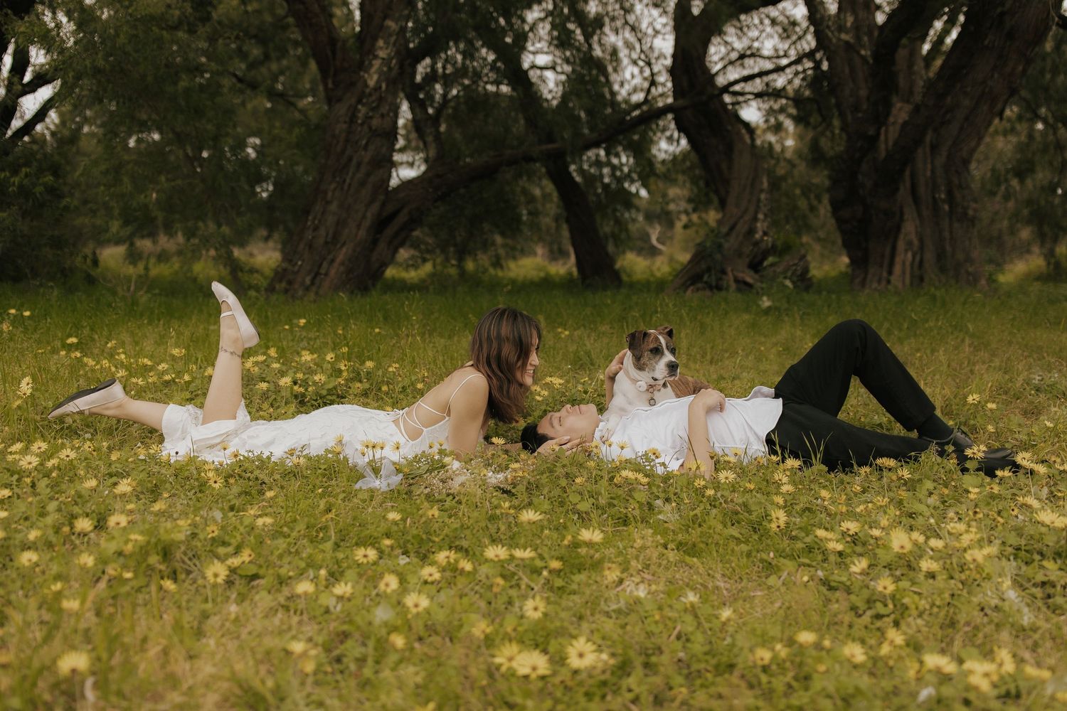 A couple runs through a grassy field scattered with yellow flowers on a sunny afternoon.