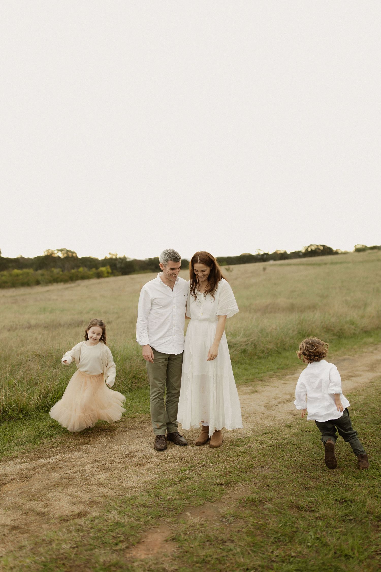 Family walking along a grassy path in a golden field during a sunset photo session.