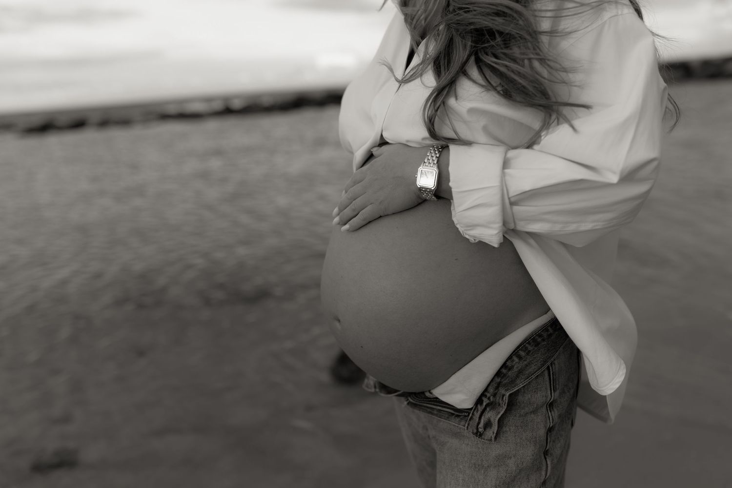 Black and white photo of a pregnant woman cradling her baby bump on a beach.