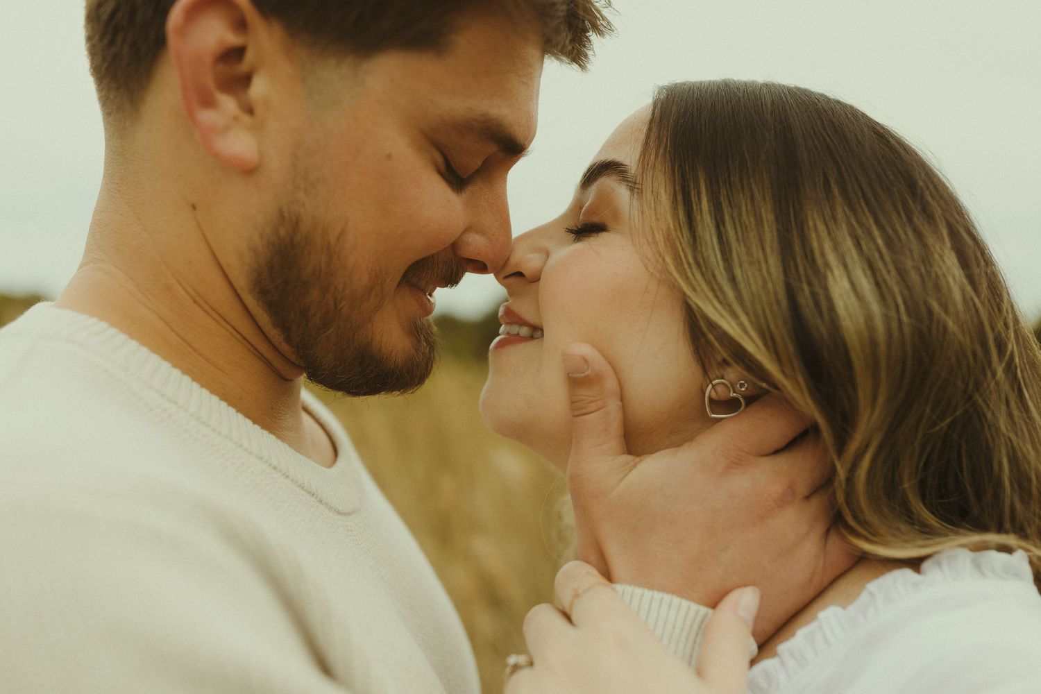 A romantic couple shares an intimate embrace in a golden-lit outdoor setting during sunset.