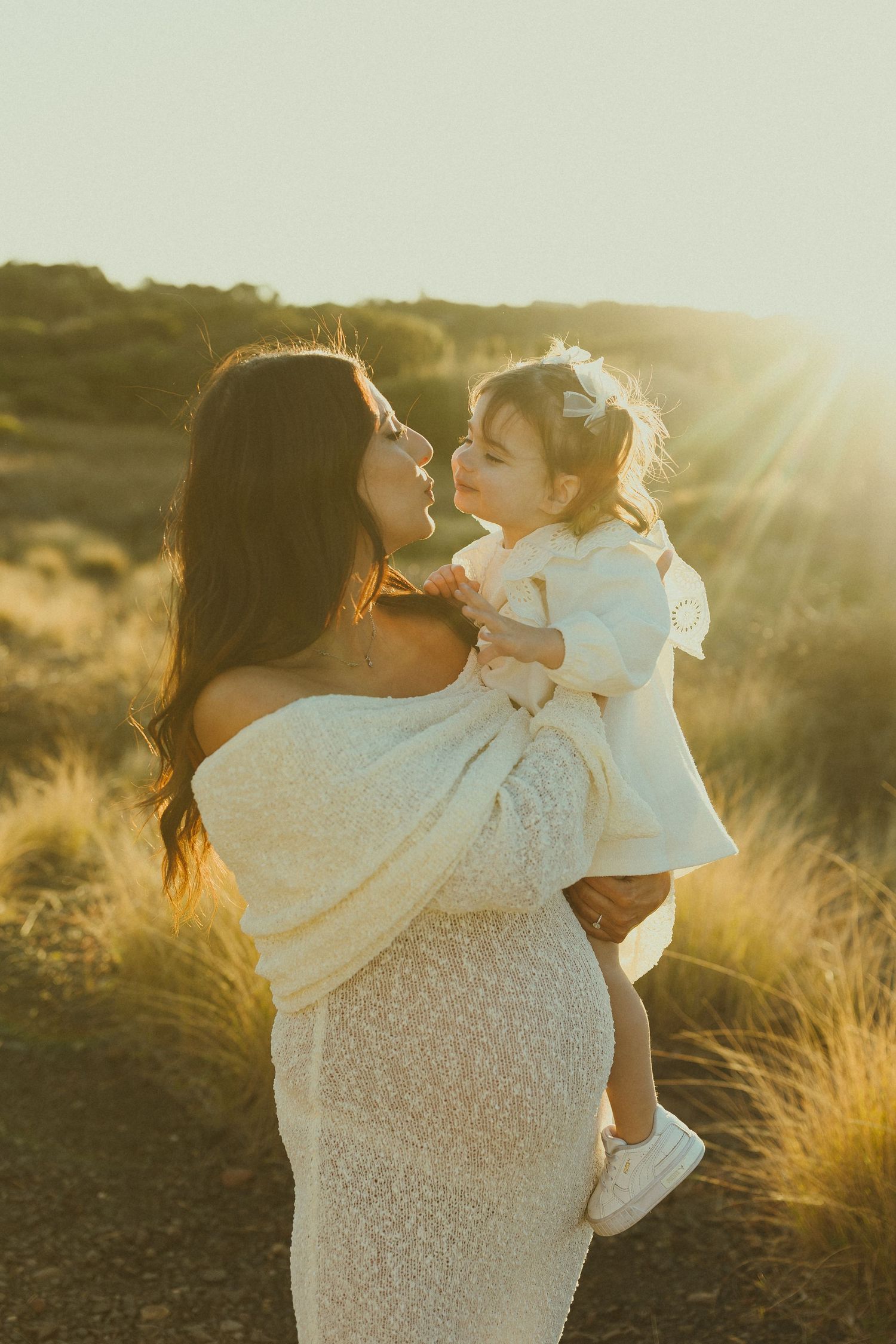 Intimate family moment captured in warm sunlight among tall grasses.