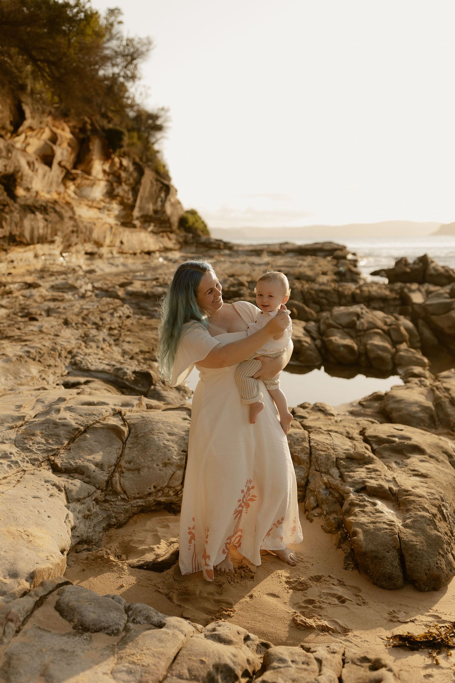 Family embraces on coastal rocks during golden hour photoshoot at the beach.