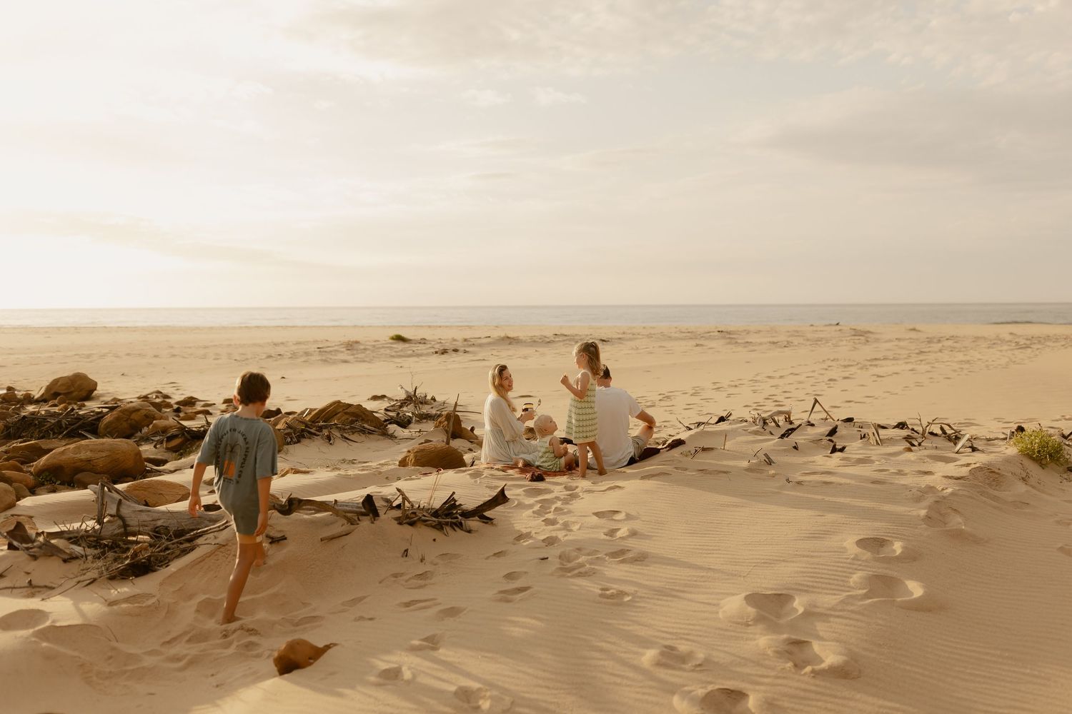 A panoramic beach scene with people relaxing among scattered rocks at sunset.