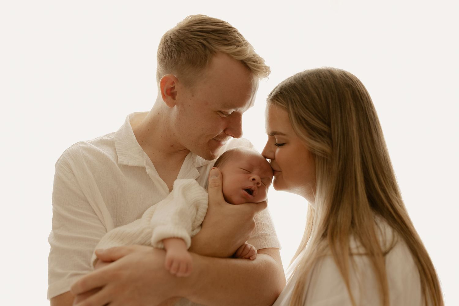 Intimate family portrait in white clothing showing loving connection and tender moments.