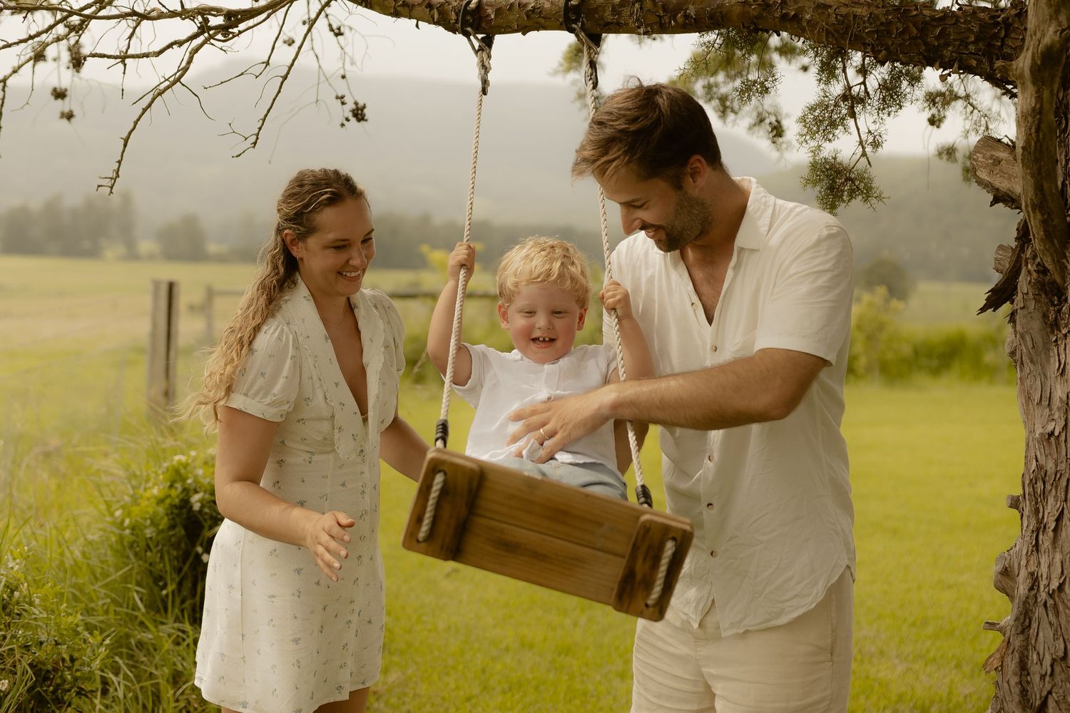 Family enjoying outdoor playtime under a tree in a countryside setting.