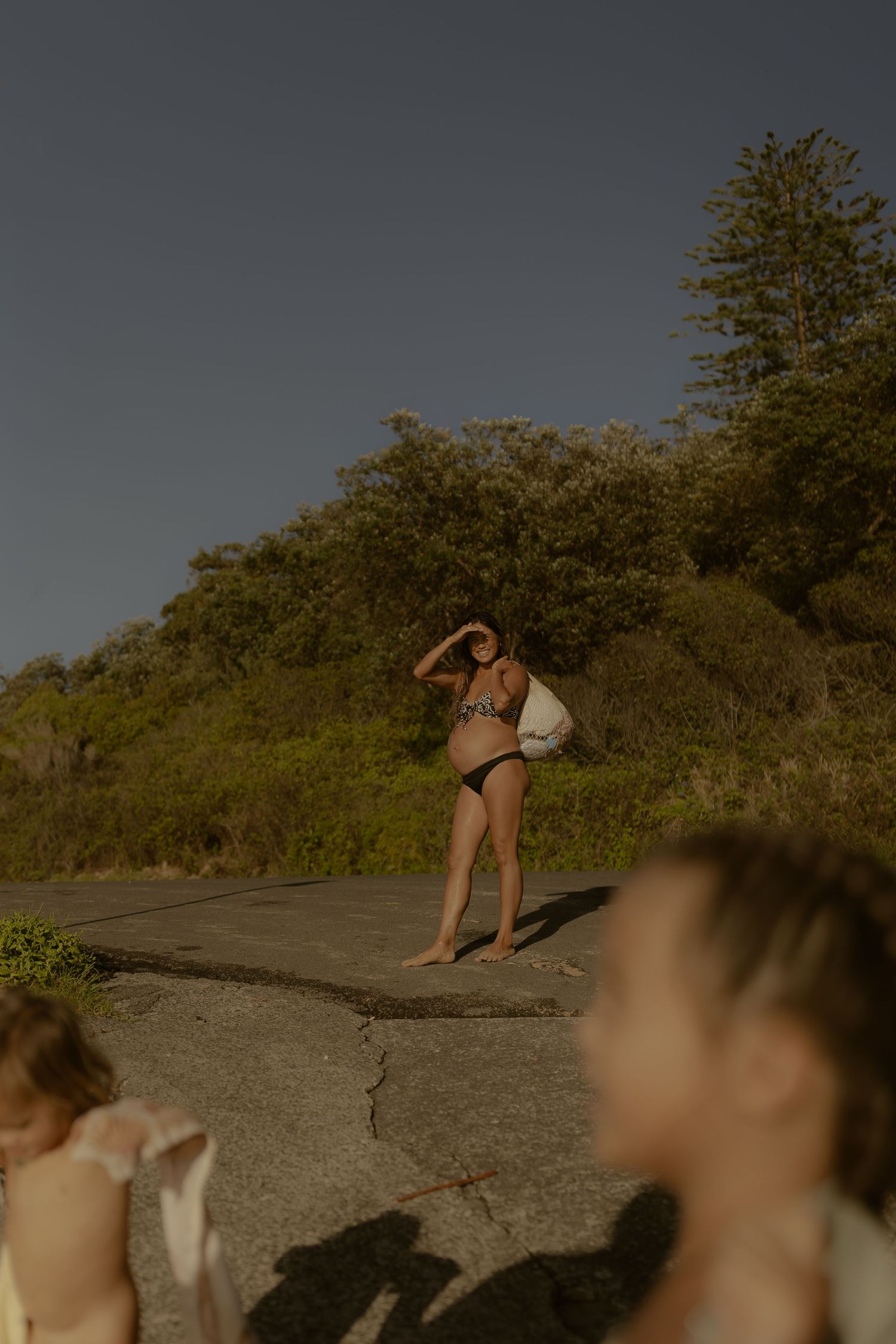 Sunlit coastal scene with people enjoying a summer day near green hillside.