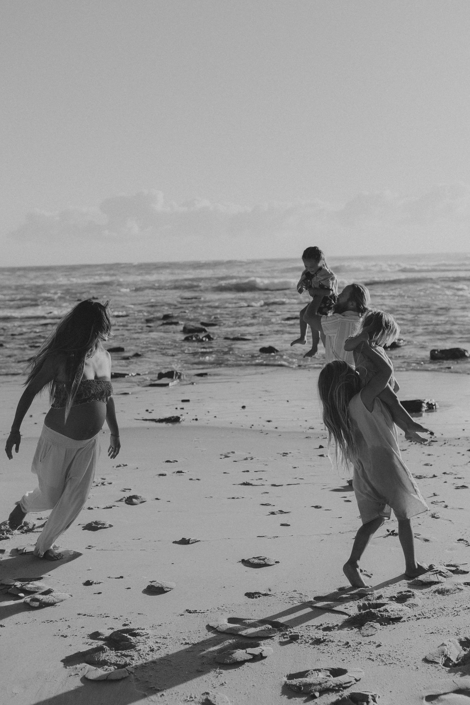 People playing and running together on a beach at sunset in black and white.