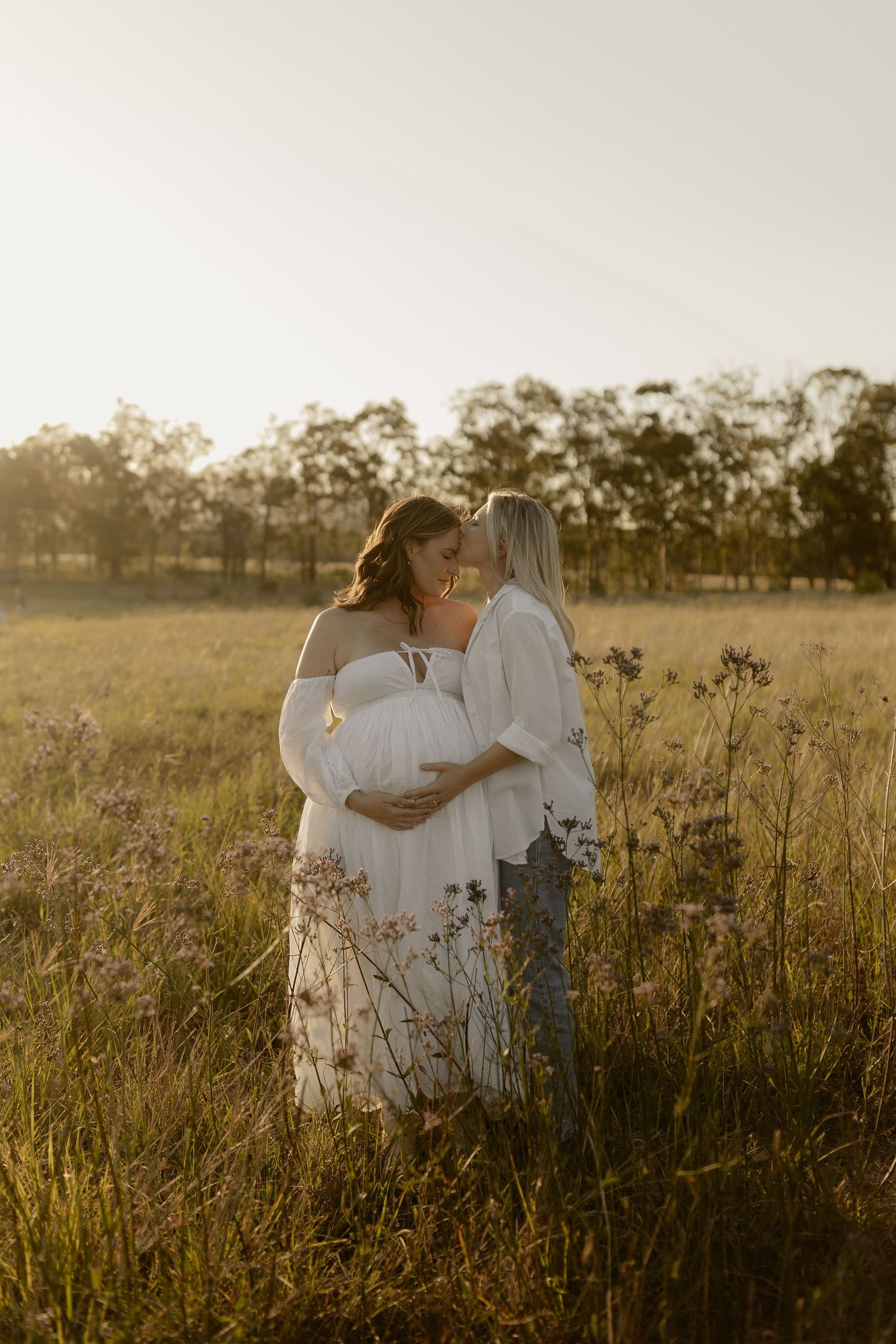 People in white dresses embracing in a sun-drenched field of wildflowers.
