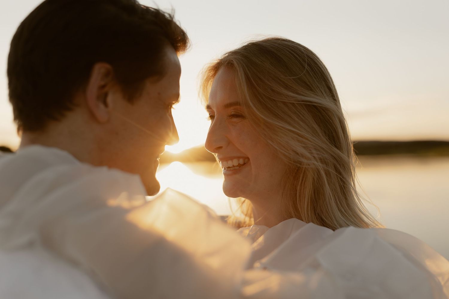 Intimate sunset moment captured between couple in white clothing by waterfront.