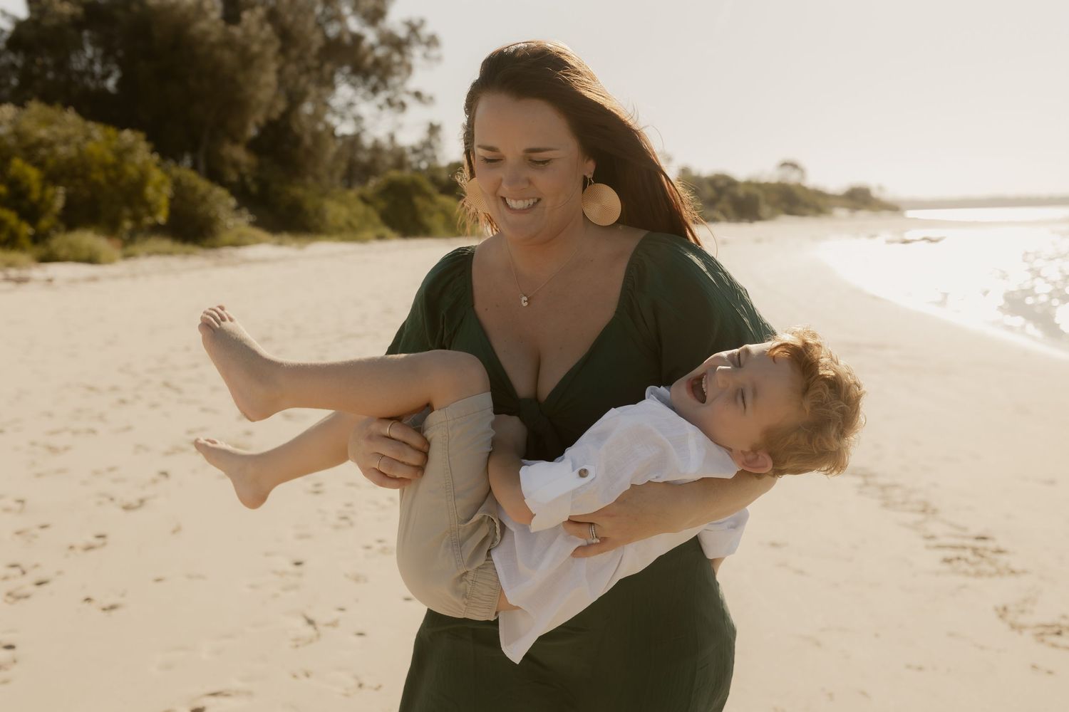 Joyful family moment captured on a sunlit beach with waves in the background.