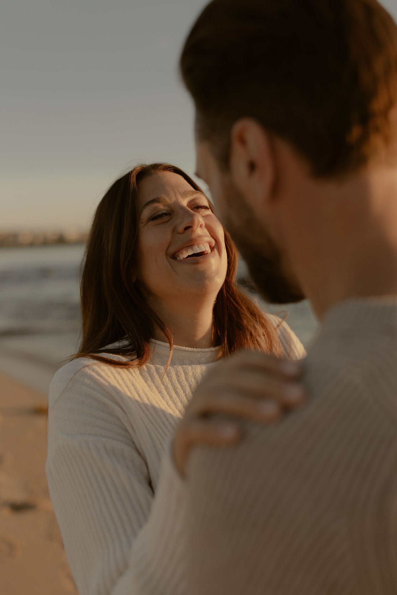 Joyful moment captured between couple on beach at sunset with warm golden light.