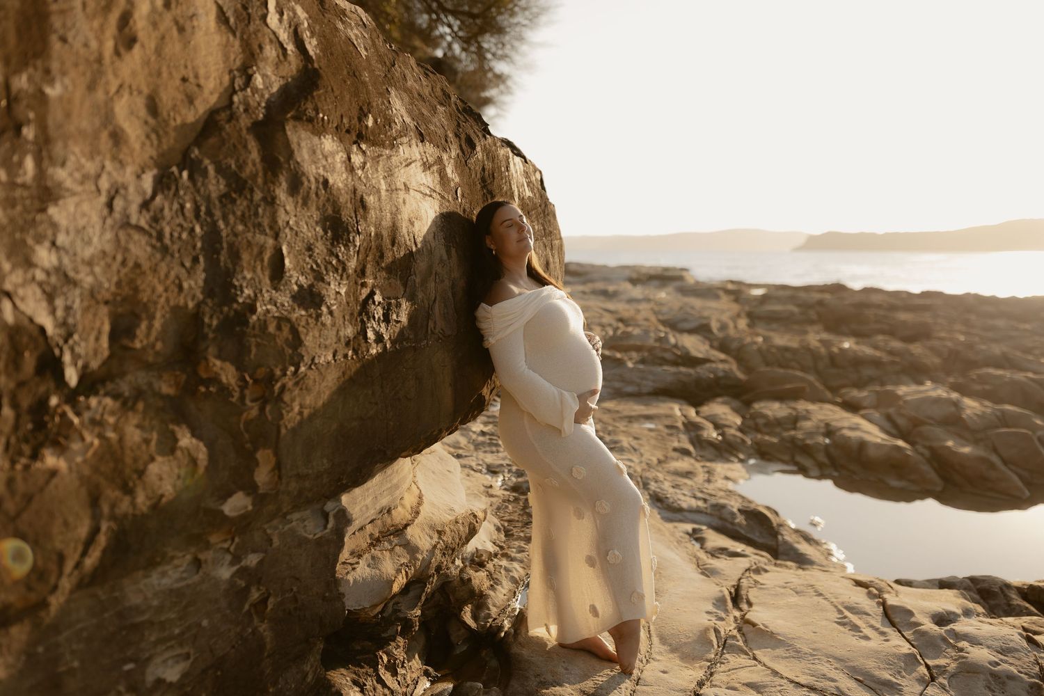 A couple sits close together on rugged coastal rocks during golden hour.