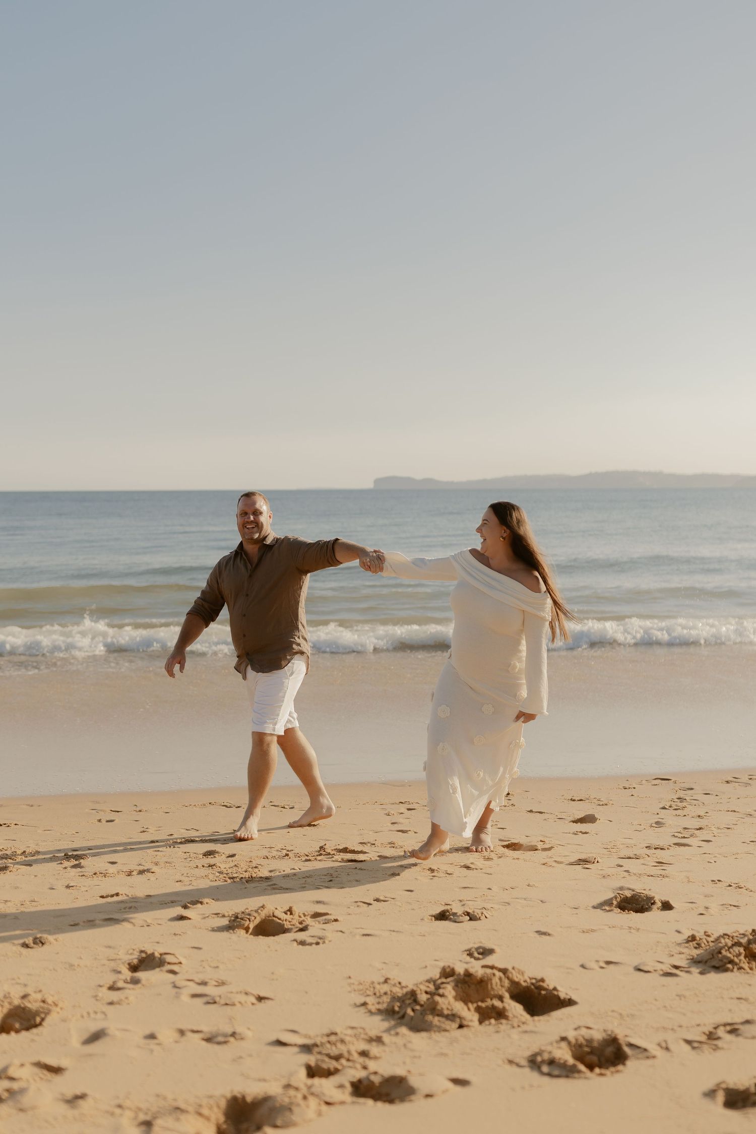 Couple walking and playing together on sandy beach with ocean waves in background.