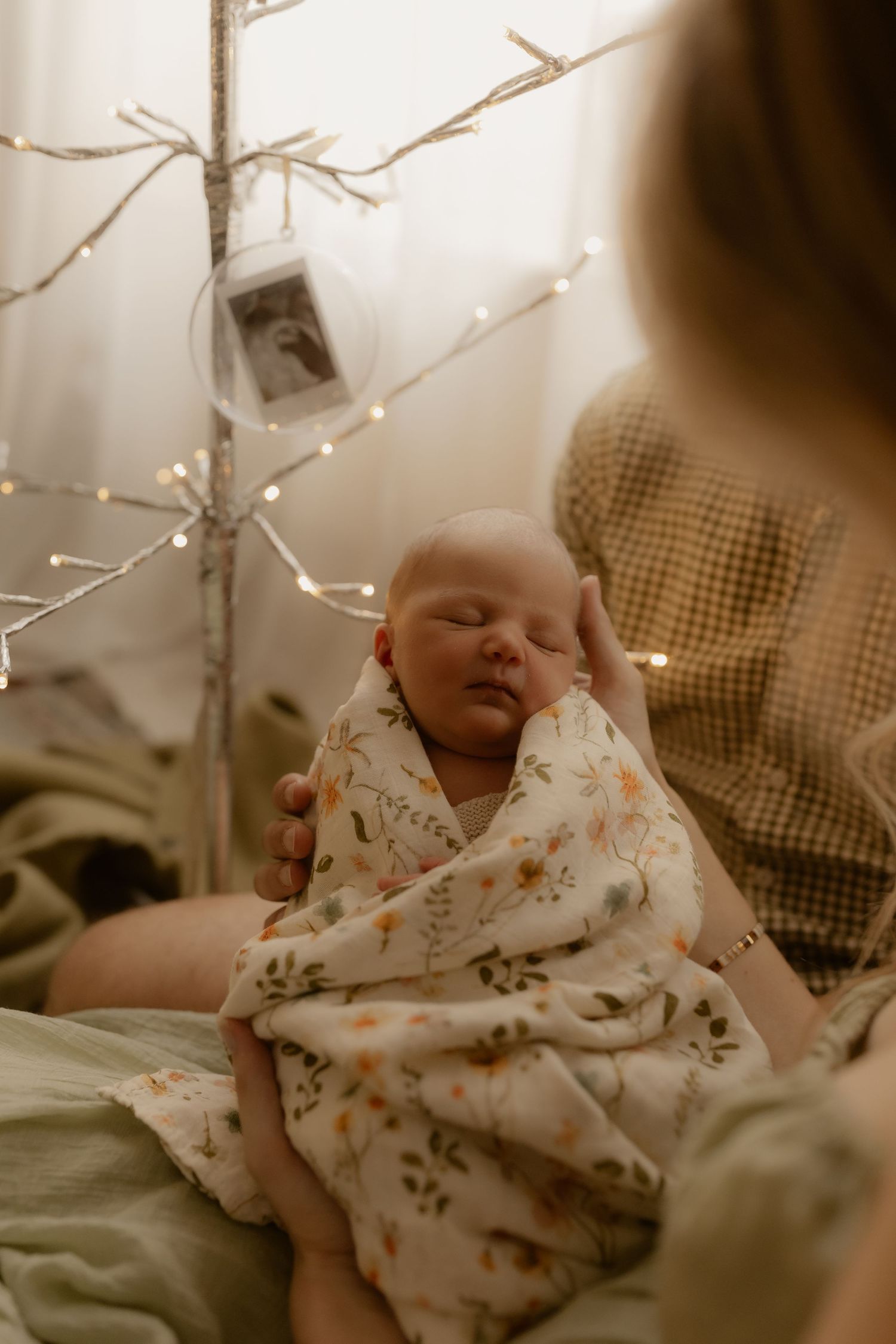 Sleeping baby in floral outfit rests under twinkling string lights.