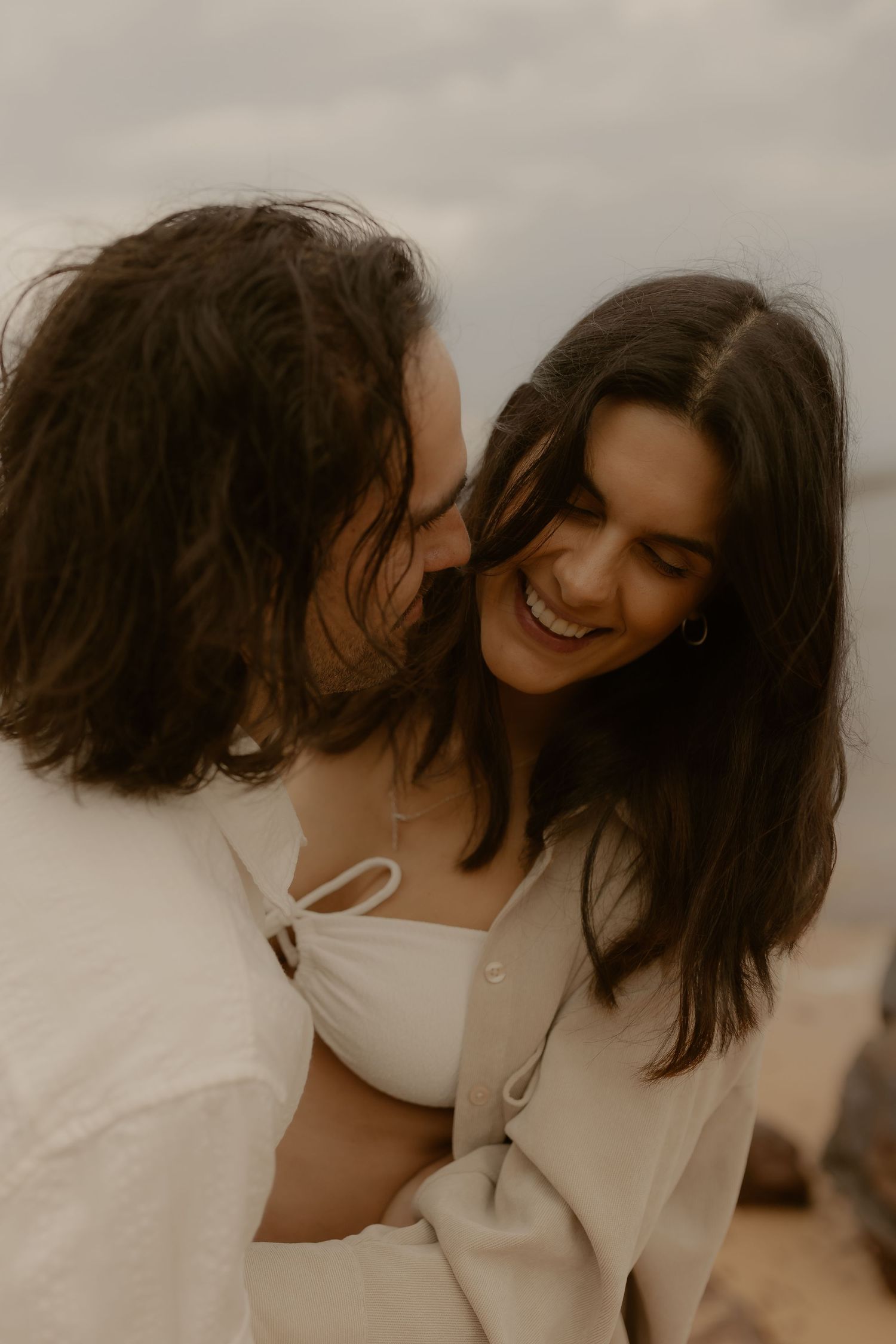 Two people in white outfits share an intimate moment against a soft neutral background.
