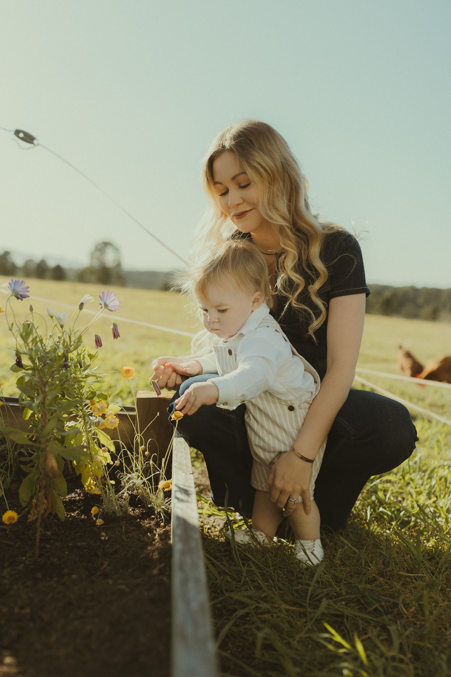 Parent and child tend to plants together in a garden on a bright afternoon.