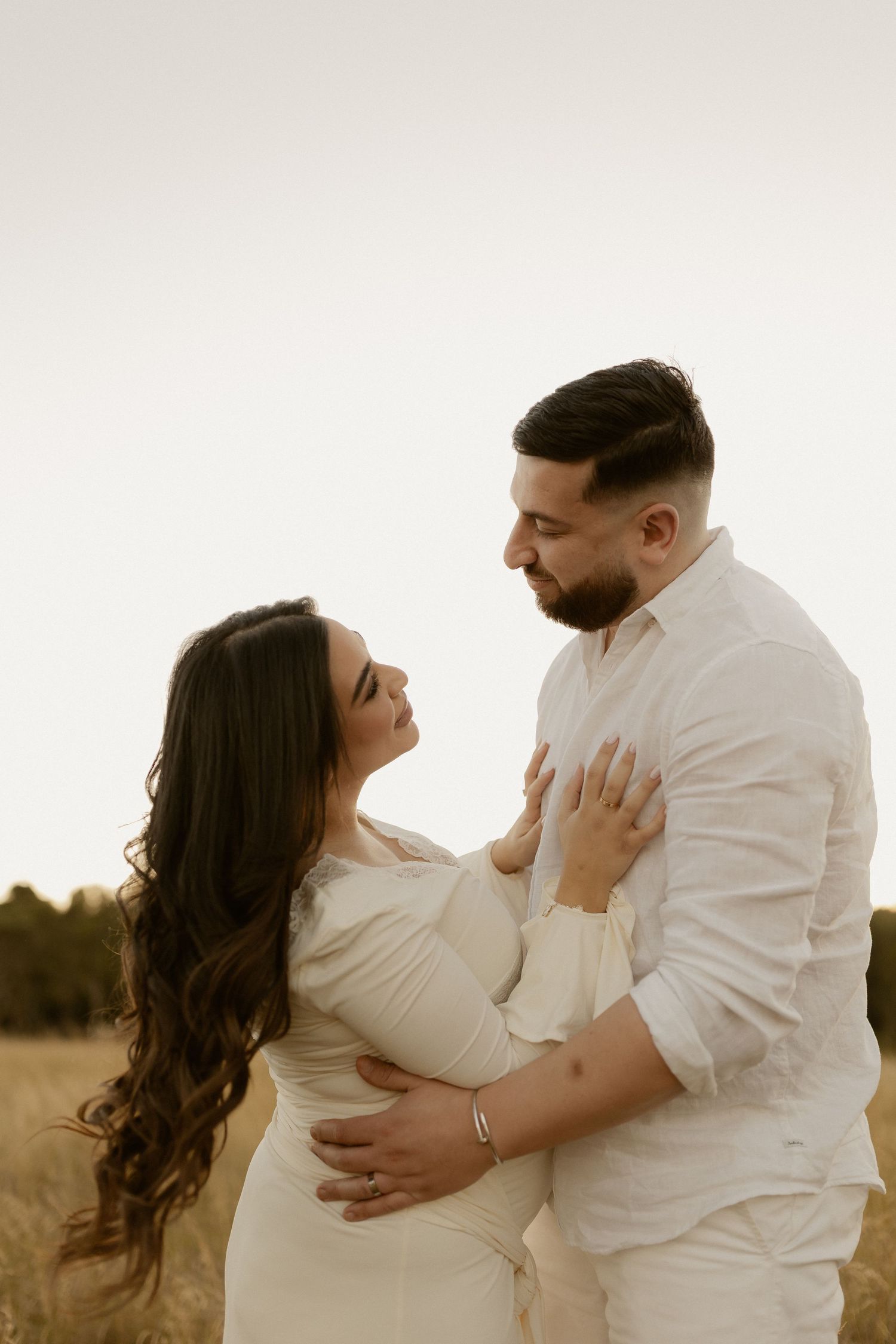 Tender moment between couple in white as they embrace during maternity photoshoot.