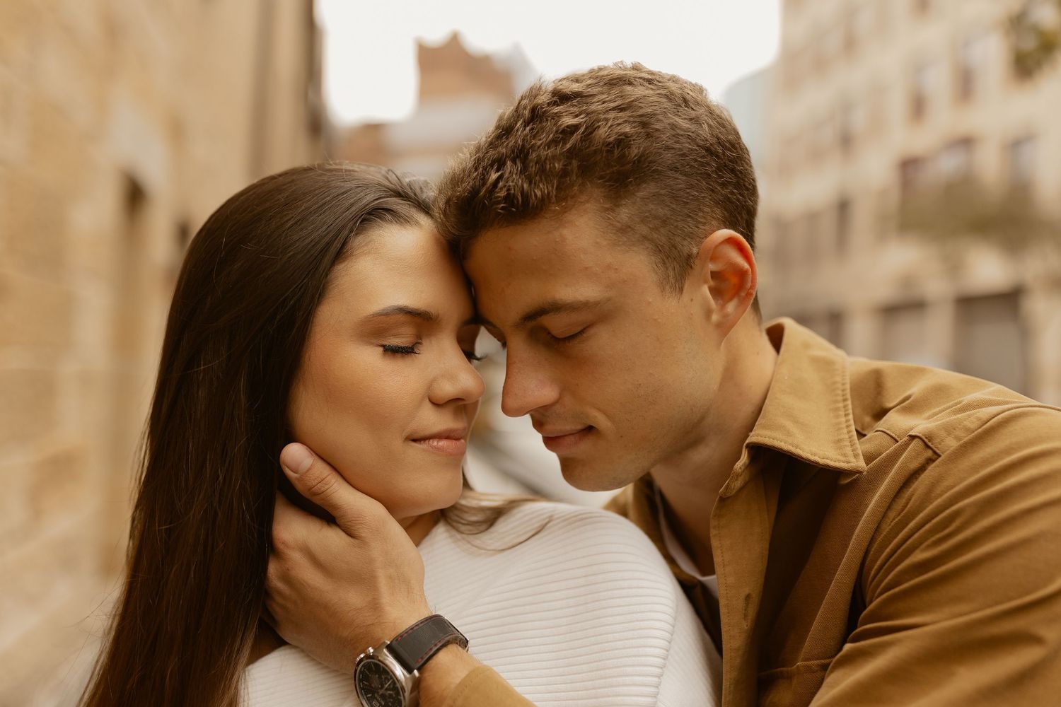 Couple in sepia tones sharing intimate moment on urban street with soft lighting.