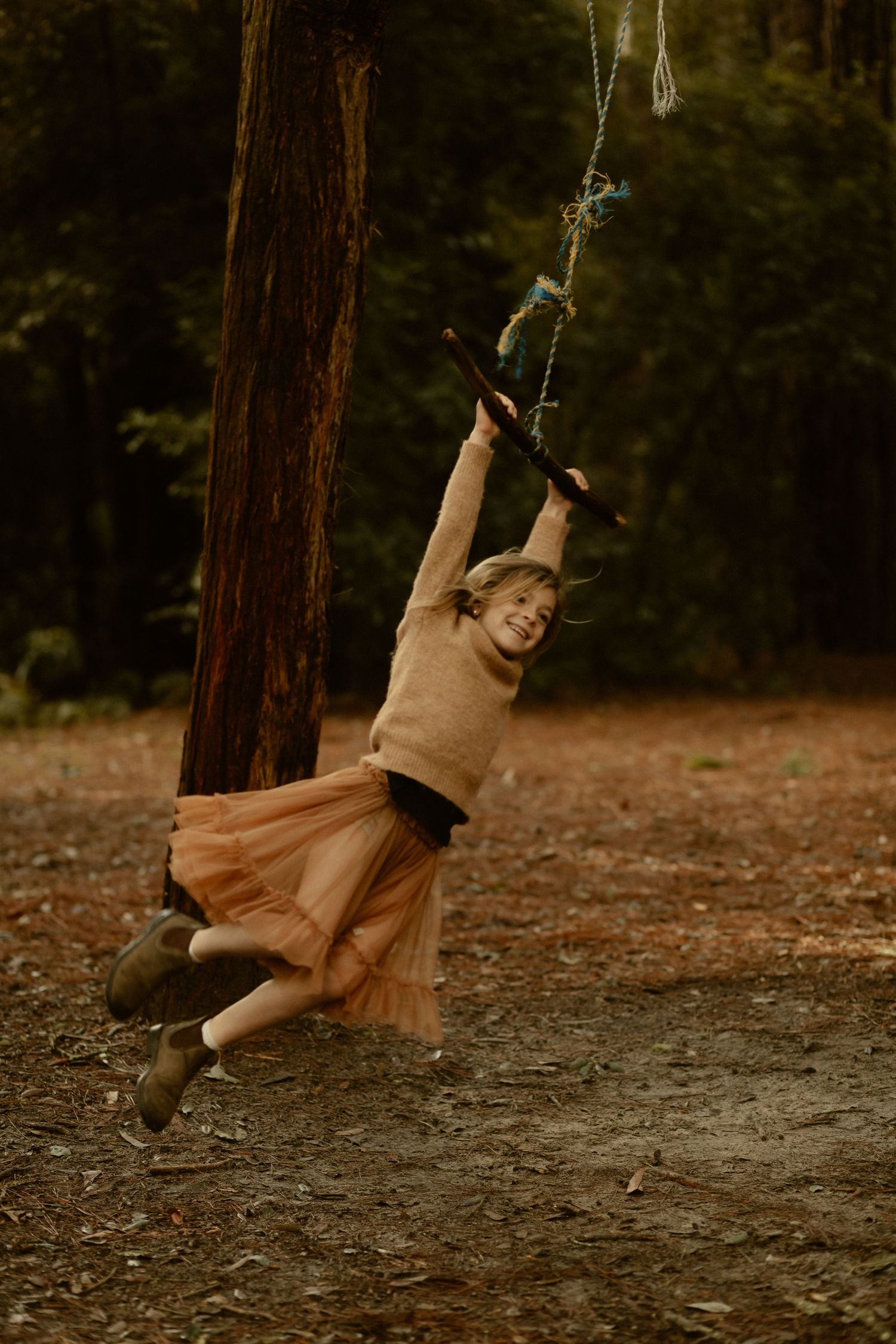 Child swinging joyfully on a rope swing in a rustic forest setting.