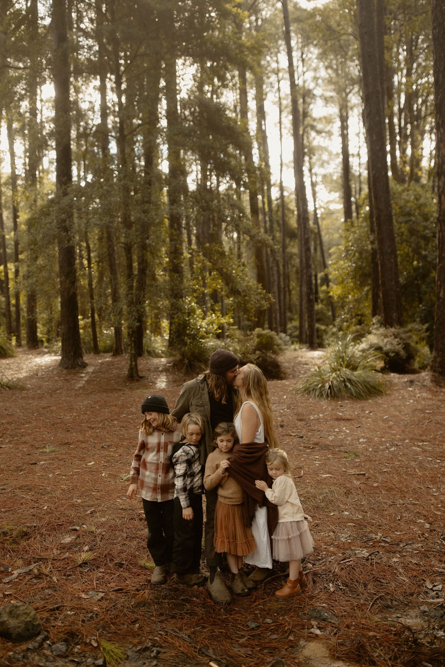 A group gathering in a sunlit pine forest wearing vintage-inspired clothing.