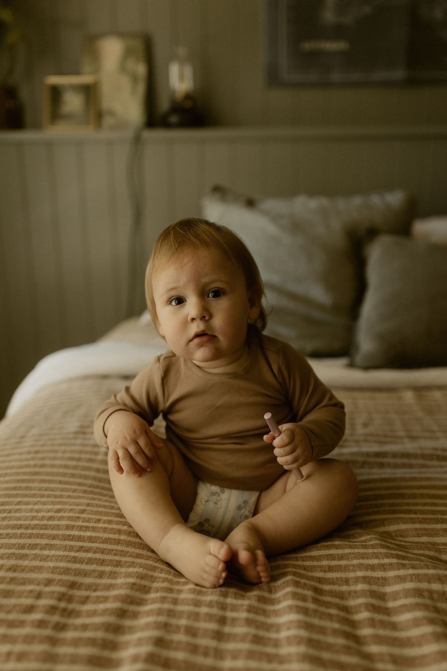 Baby in brown onesie lying on quilted bedding in natural light setting.