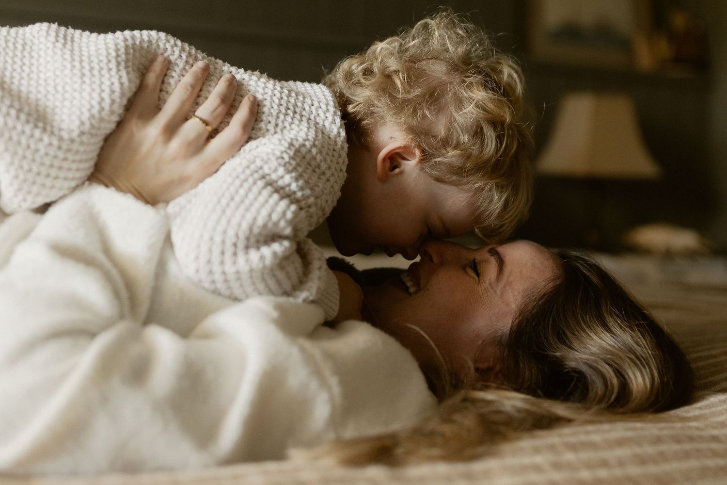 Tender moment shared between parent and young child in cozy white sweaters laying on floor at home.