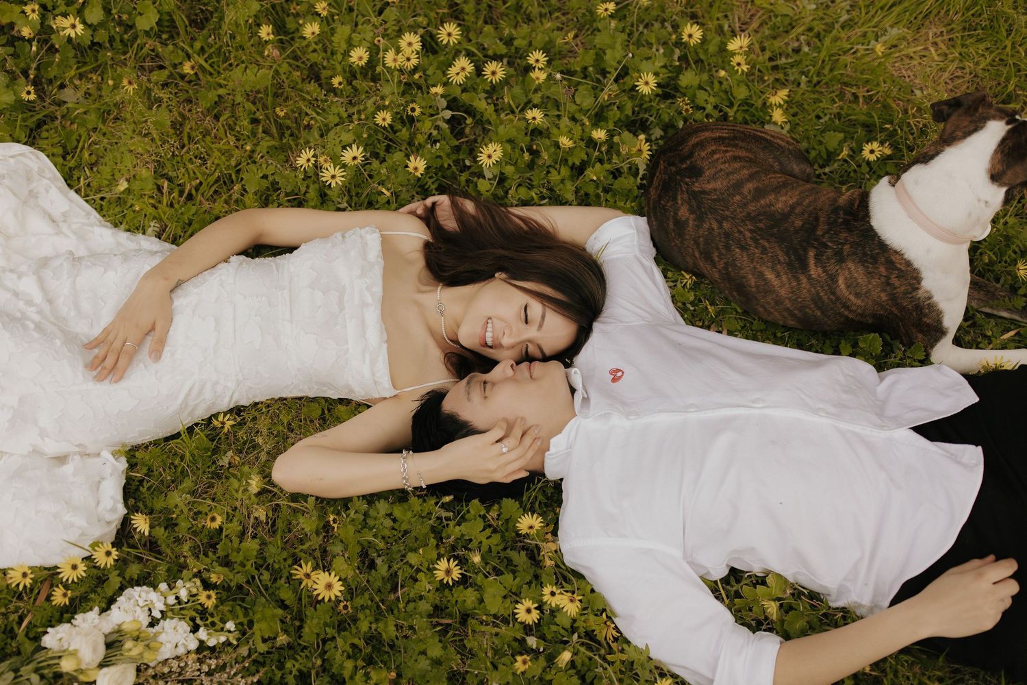 Woman in white dress reclining on grass with scattered yellow flowers in nature.