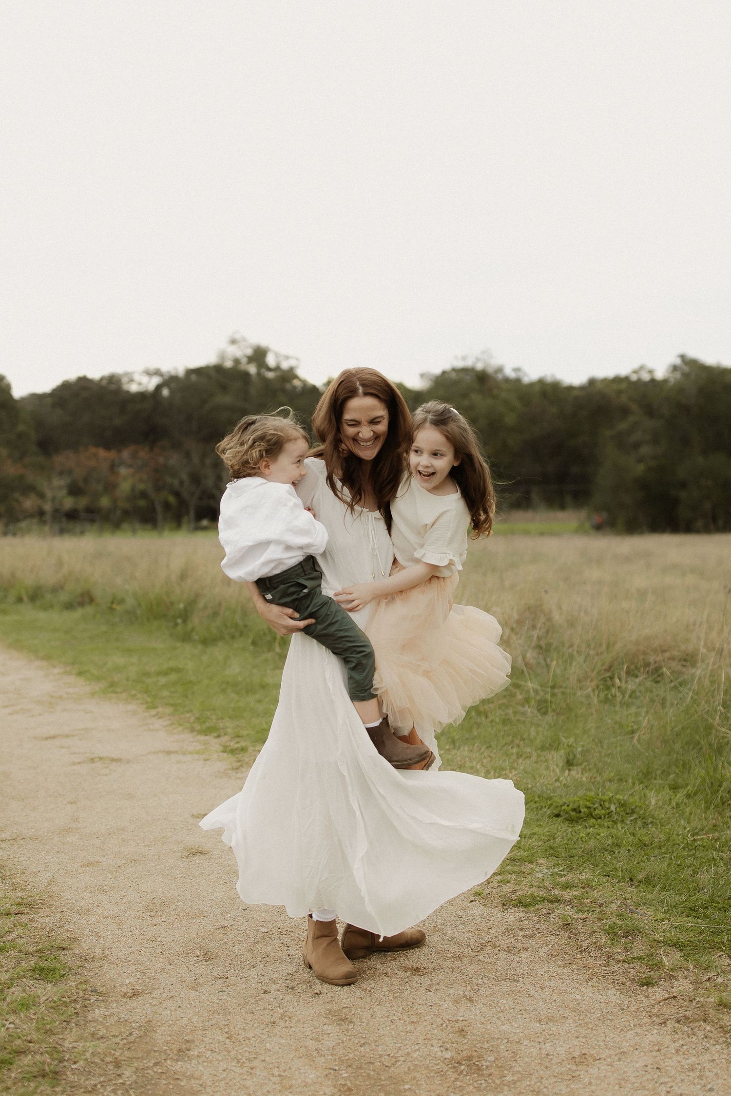 A joyful moment captured on a rustic path as people in light flowy dresses embrace and spin together.