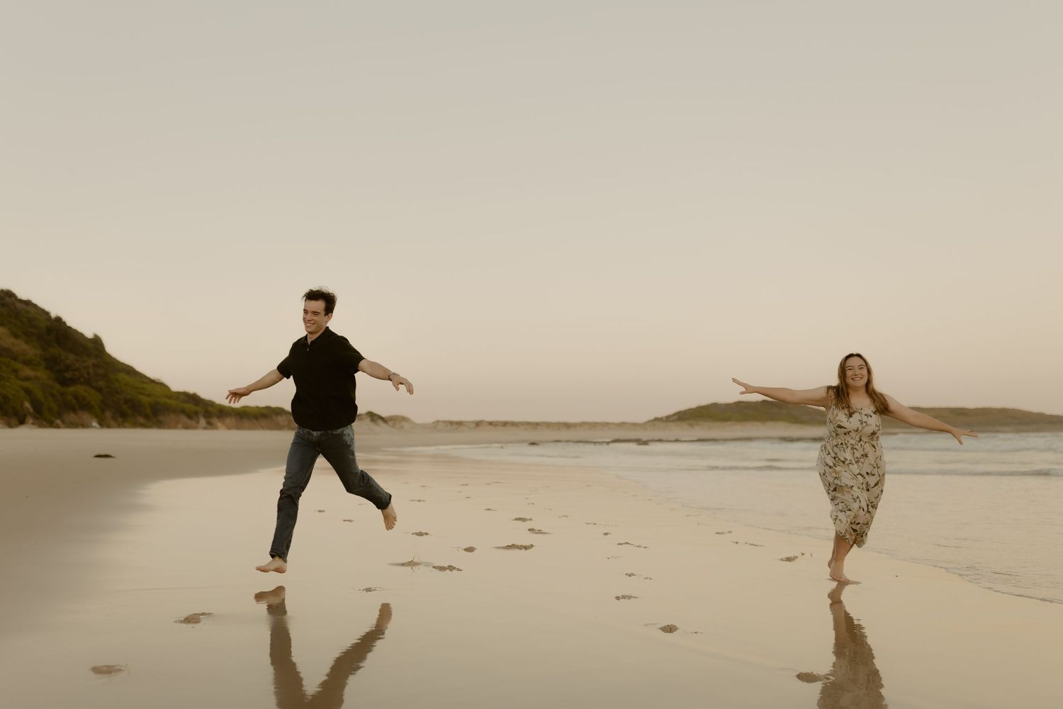 People playfully running and jumping on a wide sandy beach during golden hour.