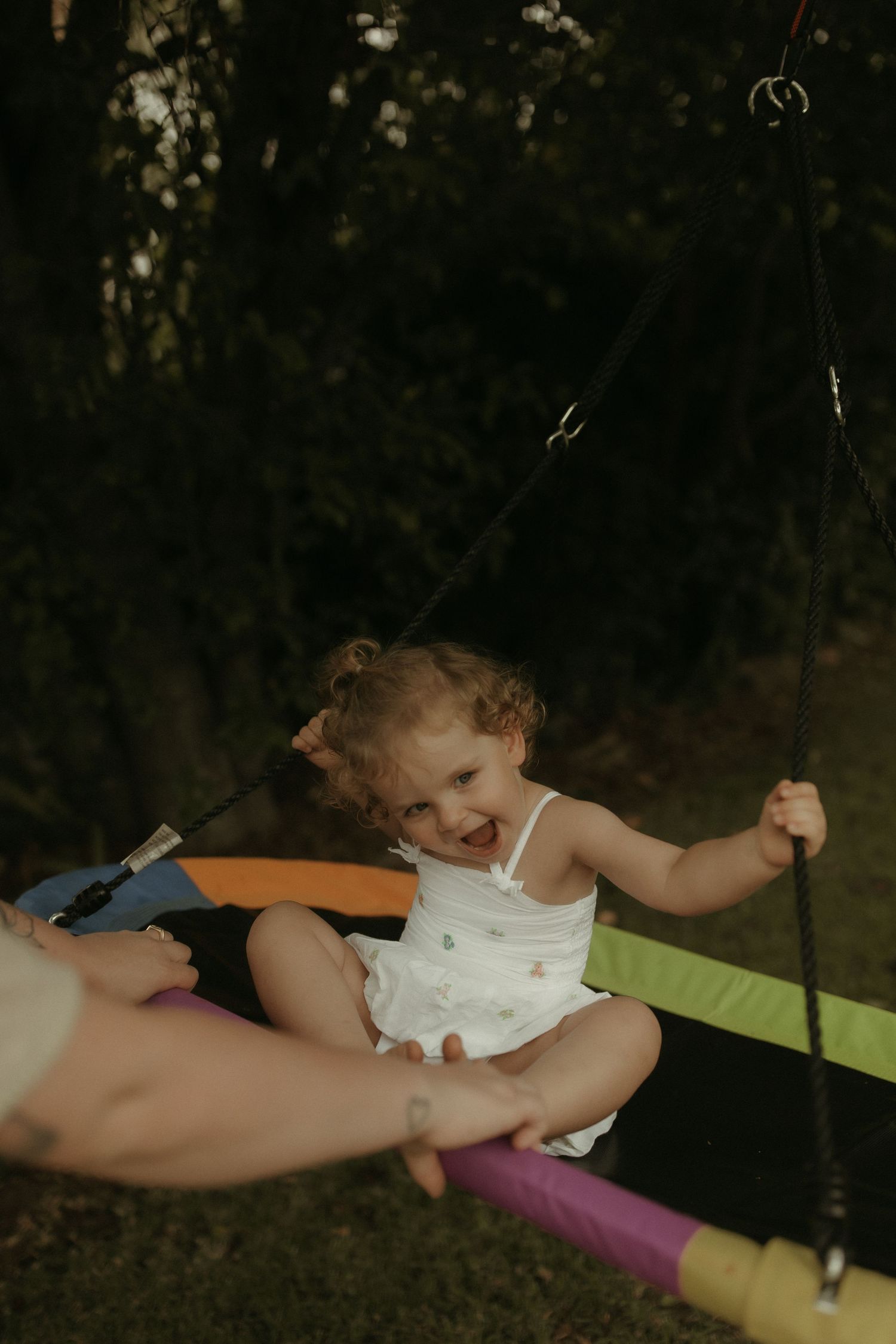 A child swings on colorful pool noodles in a backyard setting at dusk.
