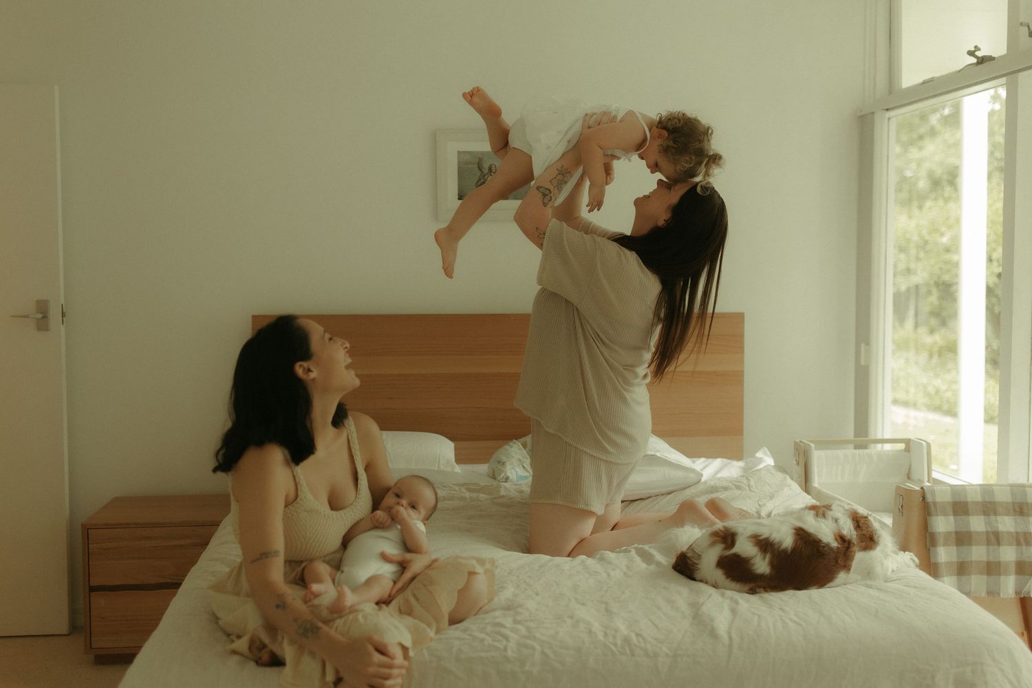 Playful interaction captured on a white bed in a bright, minimalist bedroom setting.