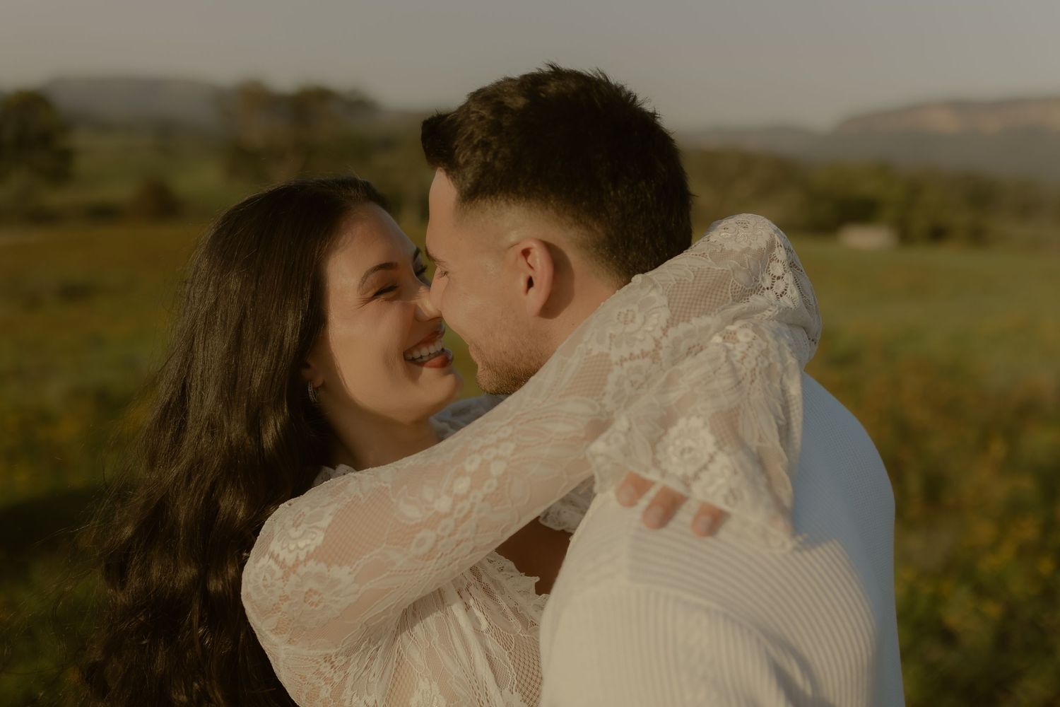 Romantic couple embraces in a golden field during sunset creating an intimate outdoor portrait.