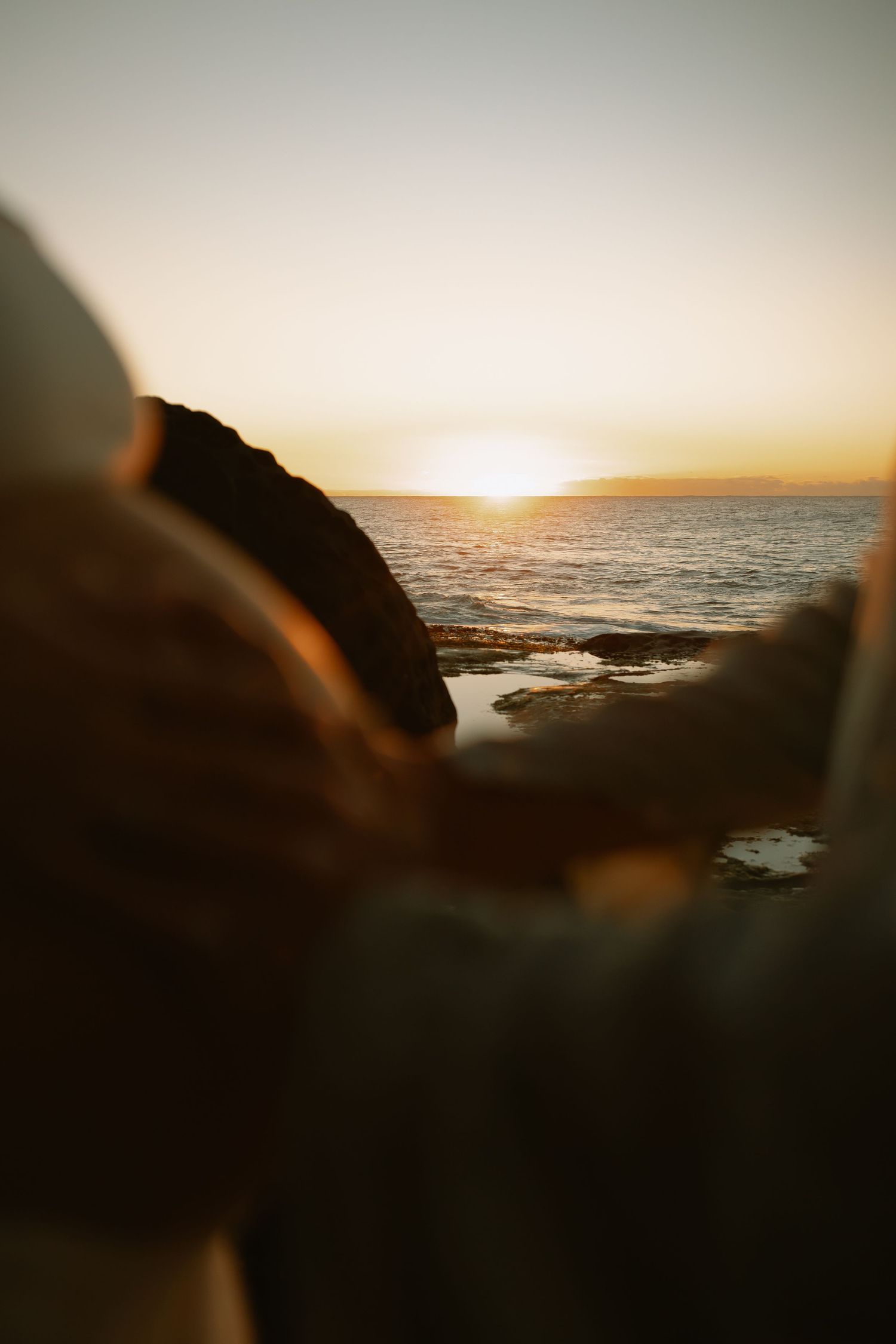 Sun setting over rocky coastline with ocean waves crashing against cliffs during golden hour.