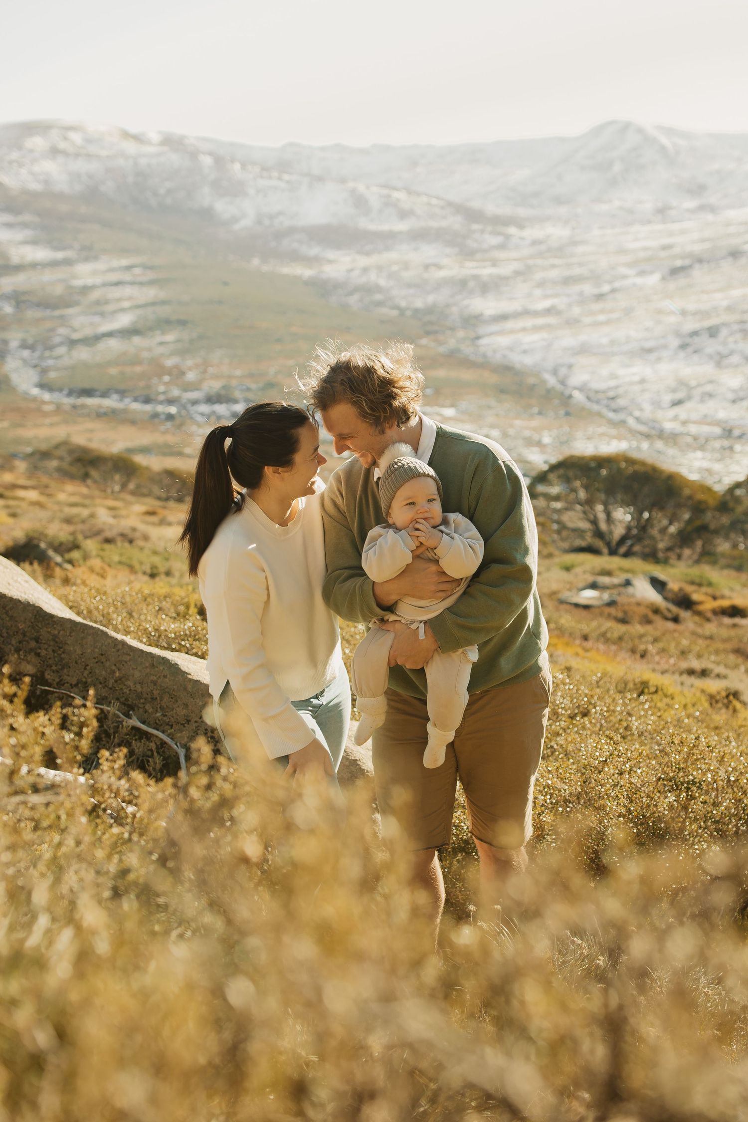 A young family sharing an intimate moment together against a backdrop of rolling mountains during golden hour.