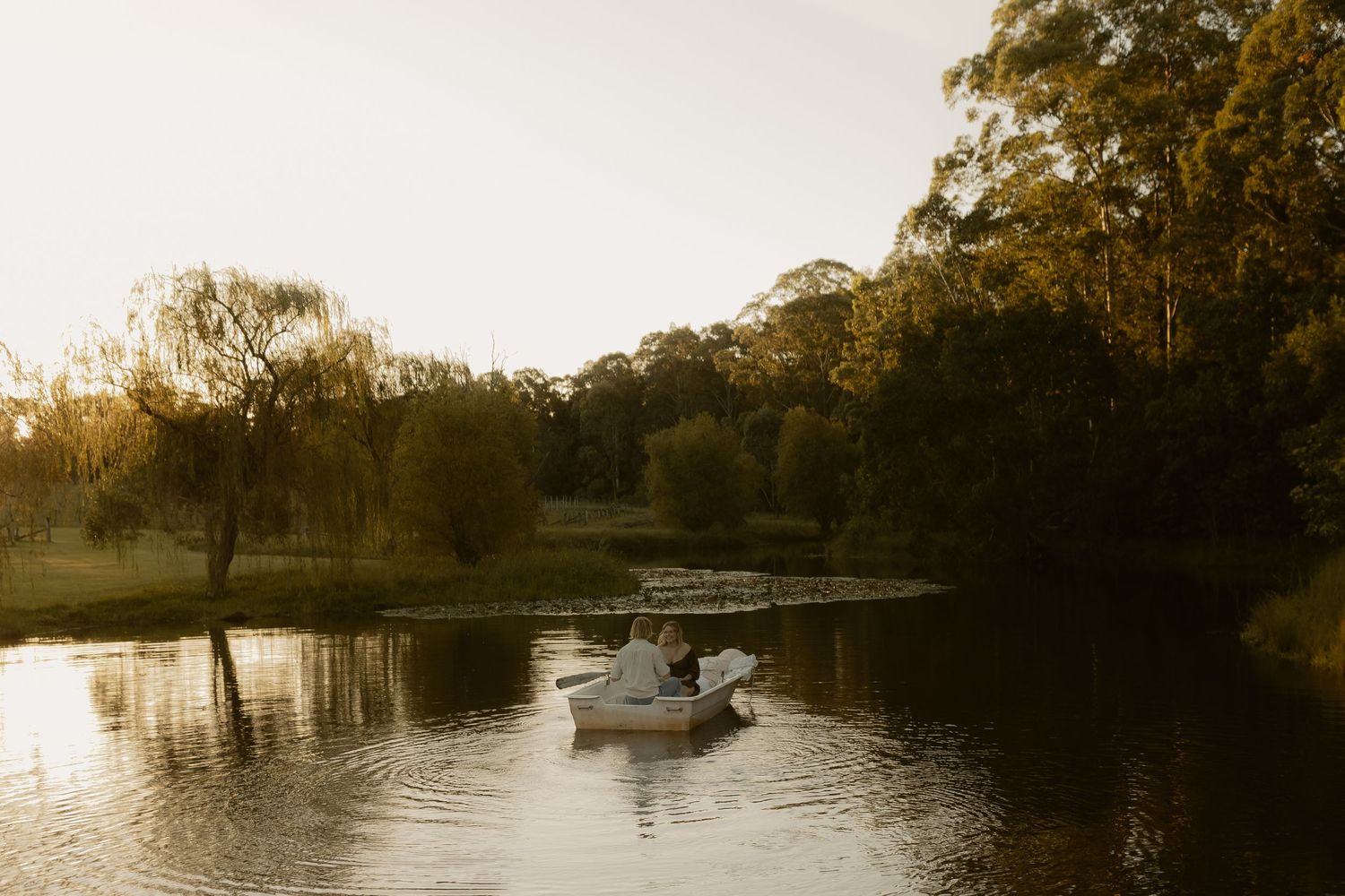 Panoramic view of a peaceful lake with boats and trees silhouetted against the evening sky.