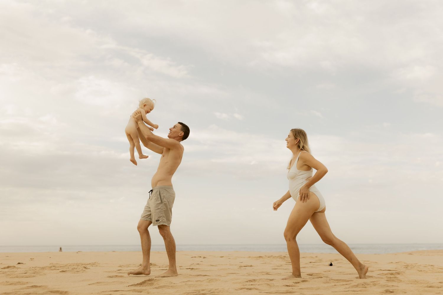 Playful figures dance and move across a sandy beach landscape at sunset creating silhouettes against the sky.