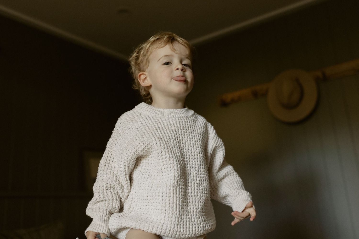 A child wearing a cream knit sweater stands in warm indoor lighting.