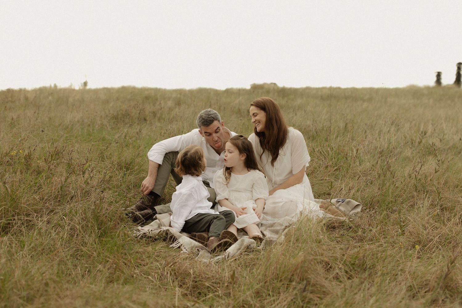A couple in vintage clothing lies on a grassy meadow with a dog during a romantic countryside photoshoot.