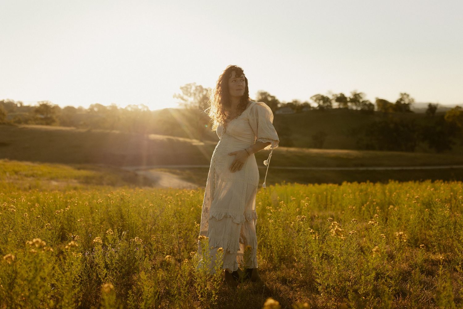 Silhouettes of a couple stand together in a golden meadow at sunset with warm backlighting.