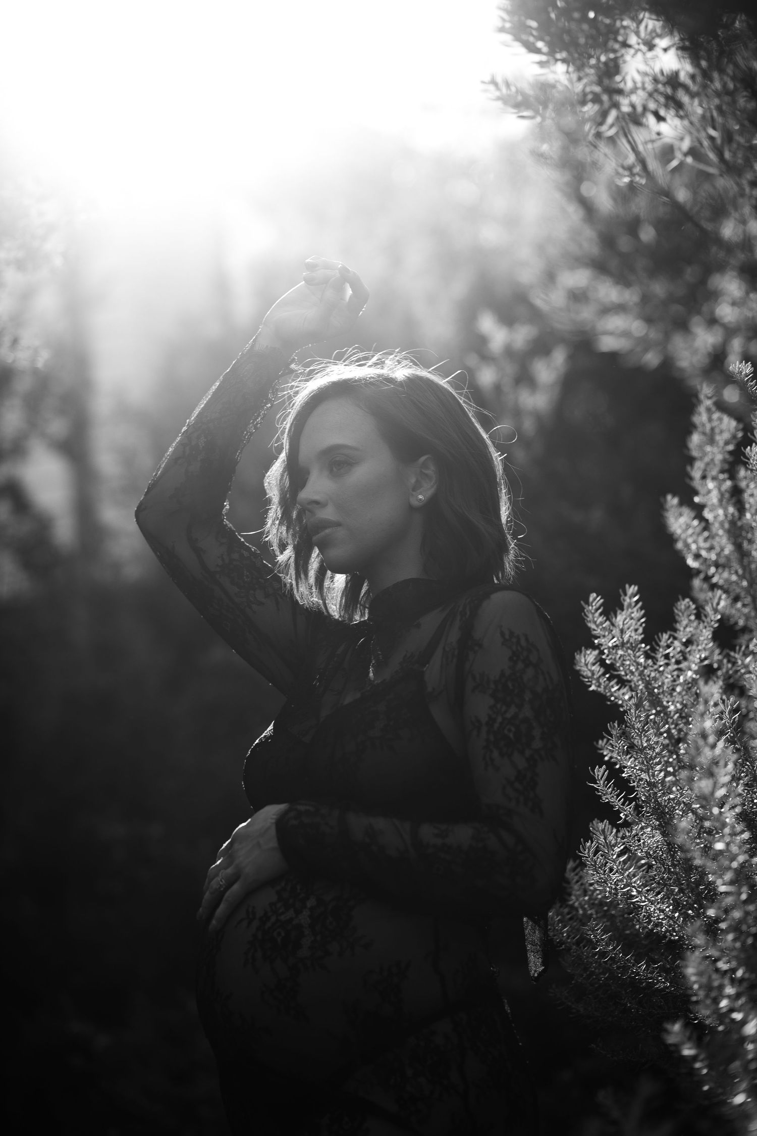 A black and white portrait of a person in profile silhouetted against sunlight filtering through trees in a dreamy garden setting.